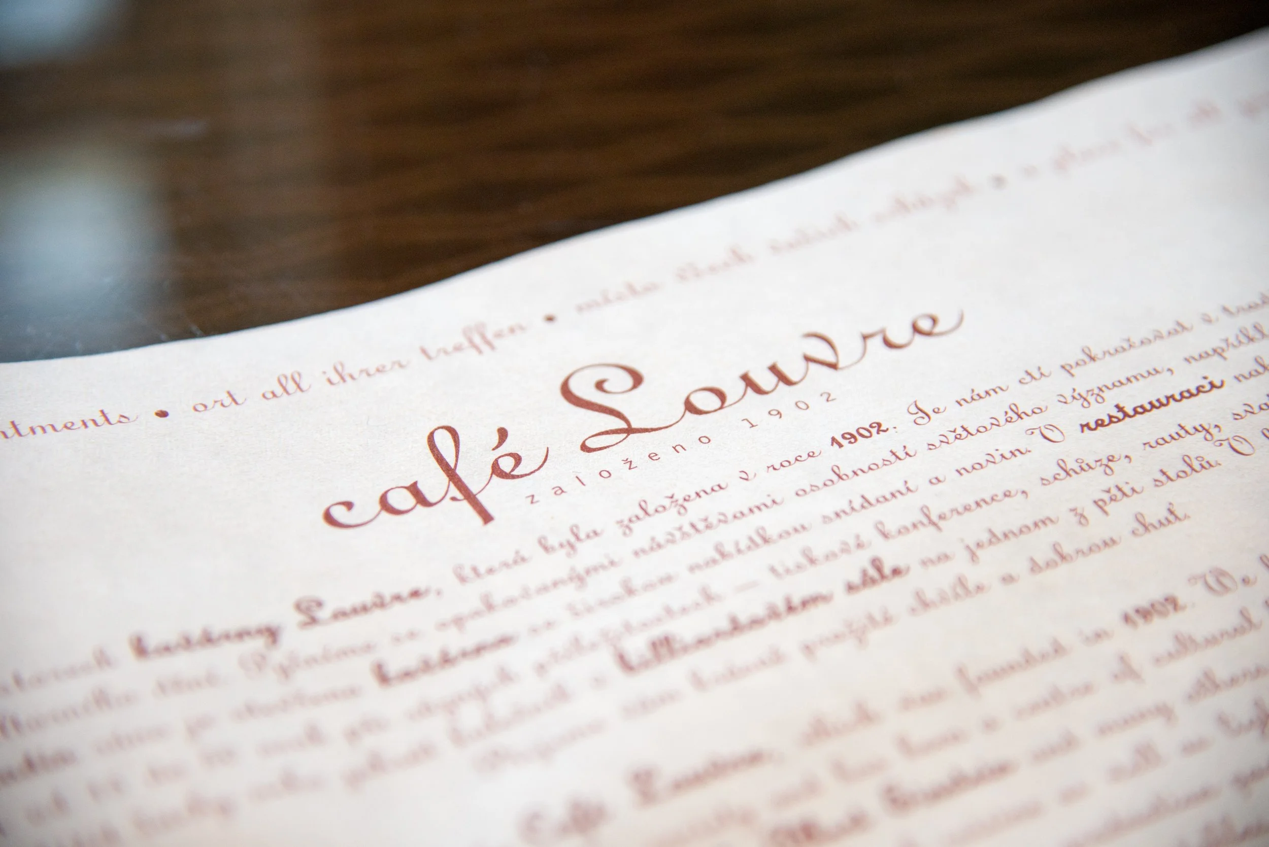 Close-up of a vintage menu or brochure page with the title 'café Source' written in elegant cursive, and a paragraph of text in a foreign language, possibly Polish.