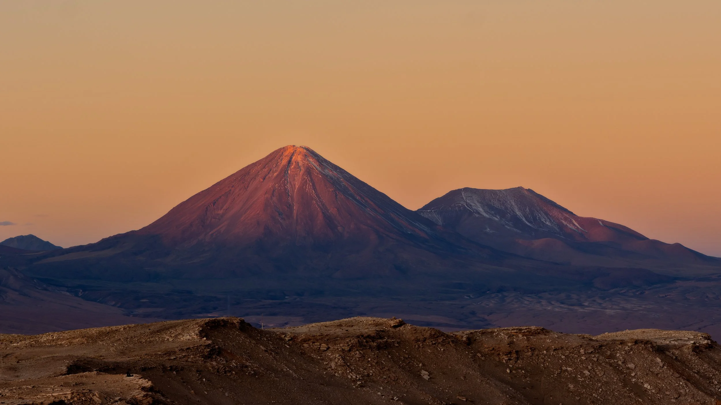 A view of two volcanoes at sunset with a colorful orange sky in the background.