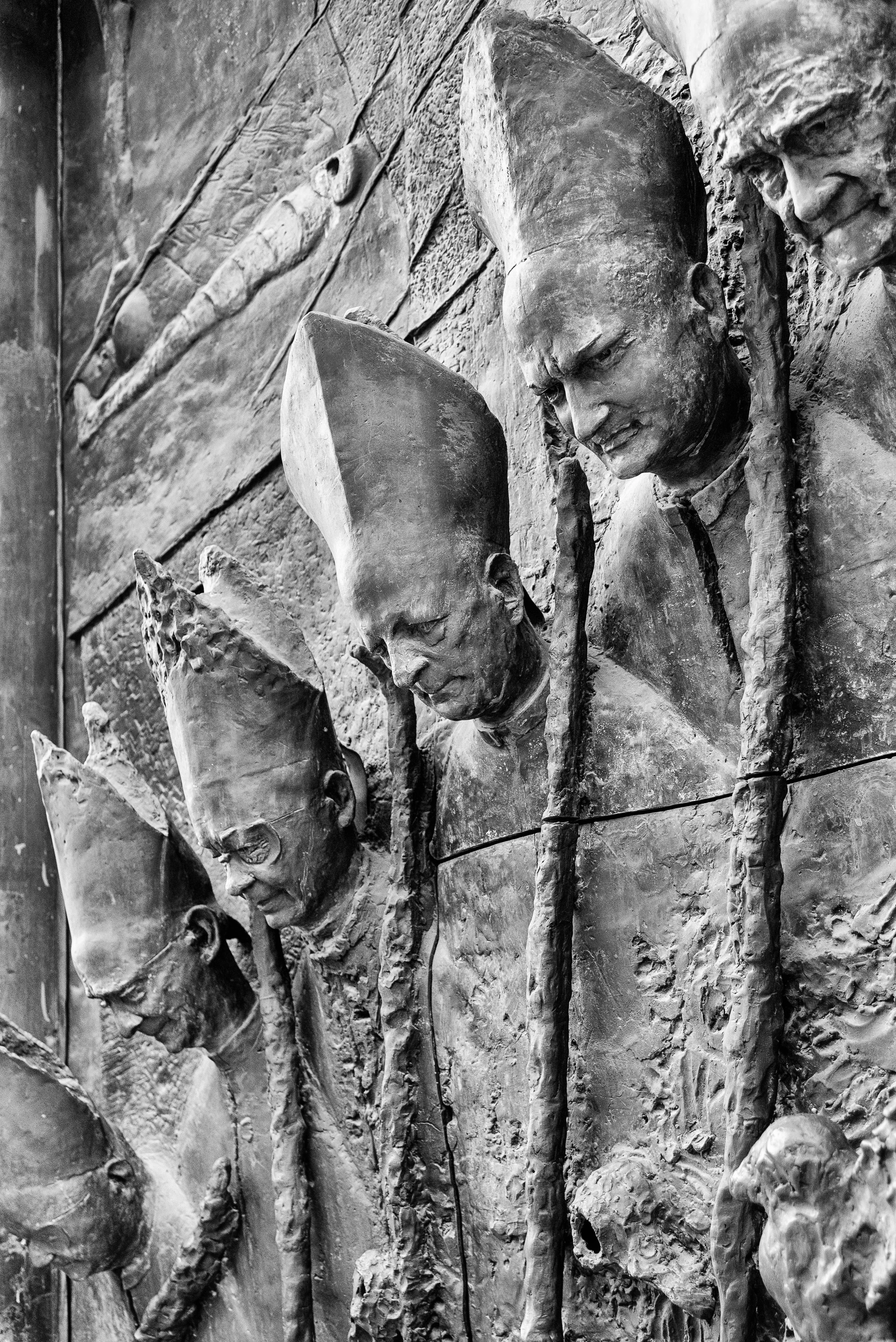 A black-and-white photograph of a bronze mural featuring seven American soldiers, some with tall hats, in a row on a textured wall.