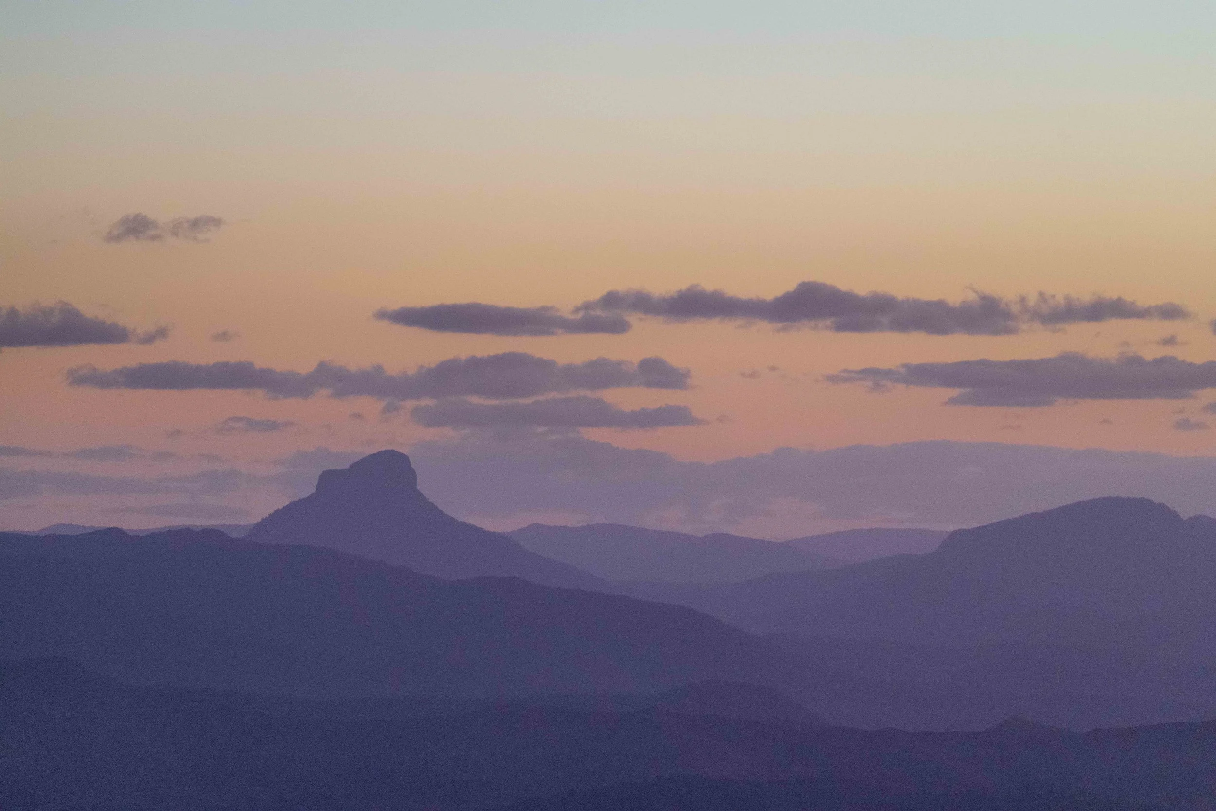 Sunset over mountain range with layered purple-blue hills and scattered clouds in the sky.
