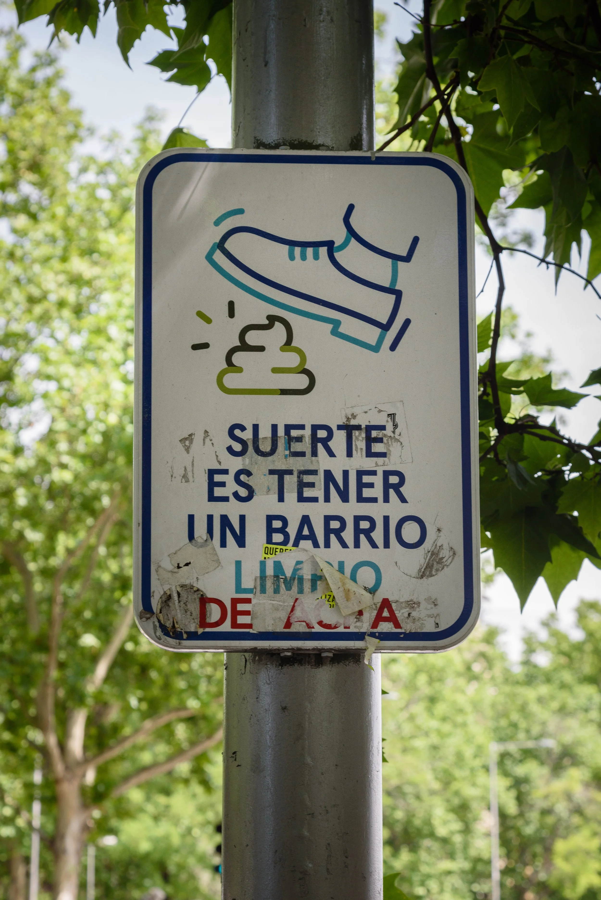 Sign with an illustration of a shoe stepping on poop and text in Spanish that reads, 'Suerte es tener un barrio limpio,' meaning 'Luck is having a clean neighborhood.'
