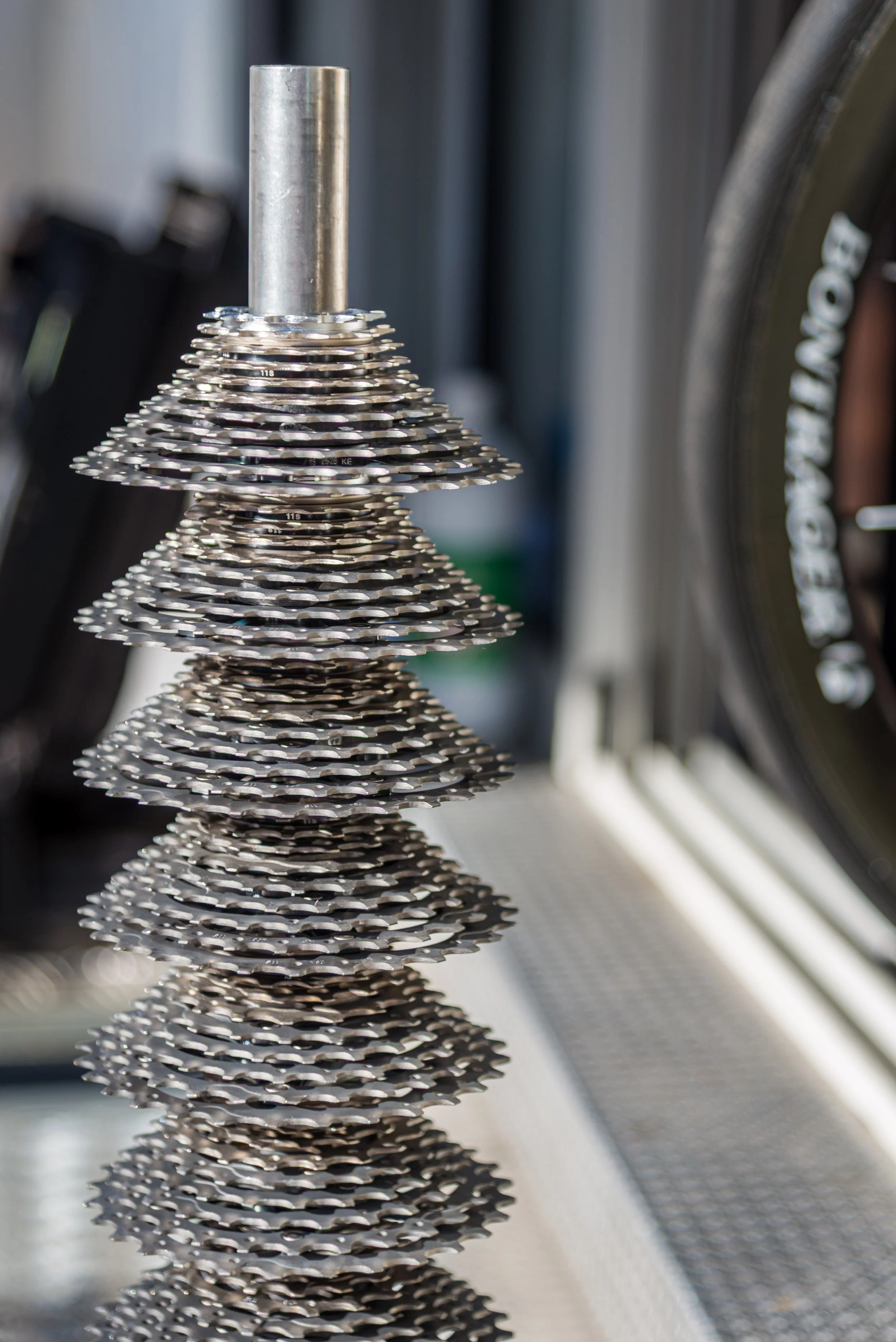 A stack of silver bicycle gears arranged in a cone shape, placed on a white surface.