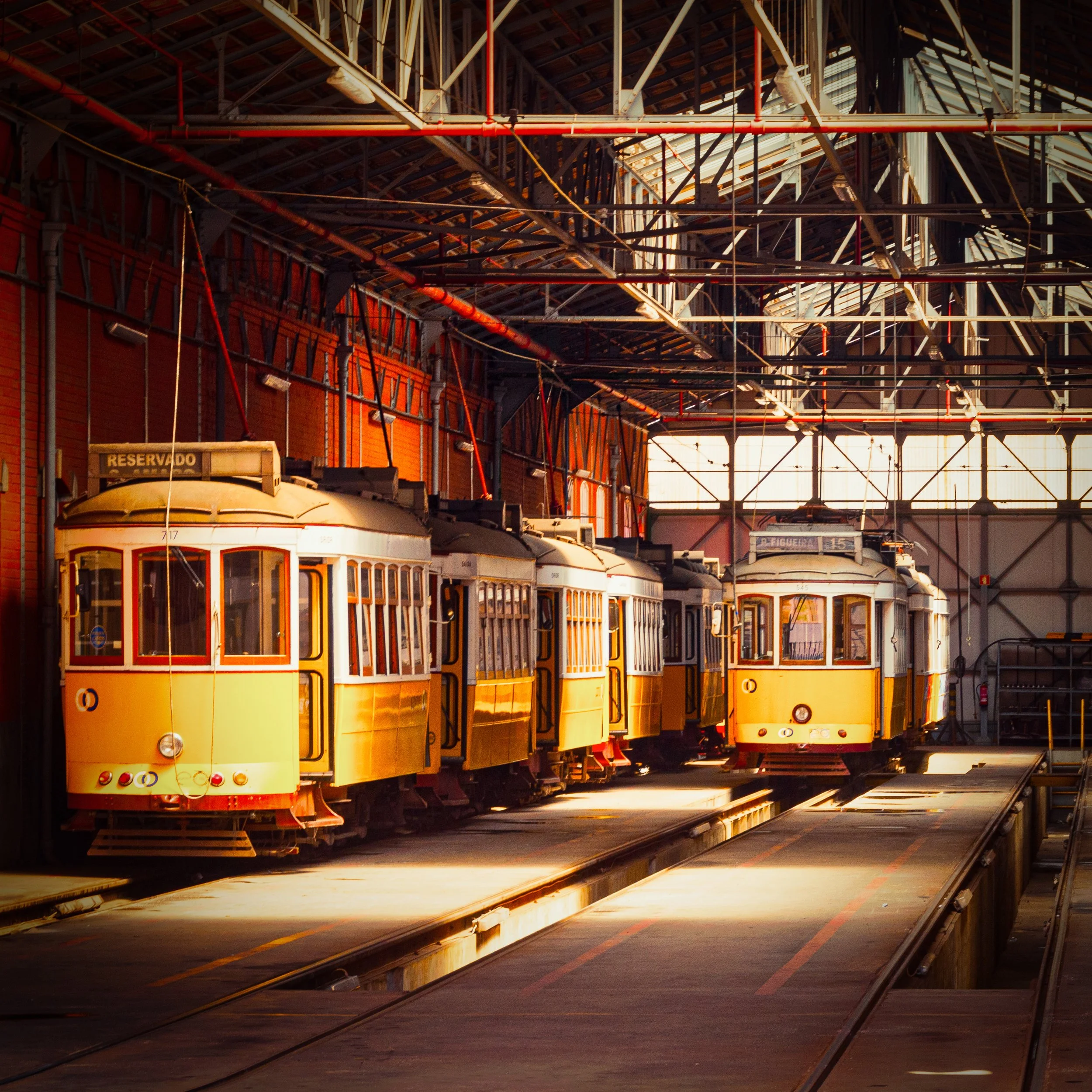 Multiple vintage yellow streetcars parked inside a train depot with sunlight streaming through windows.