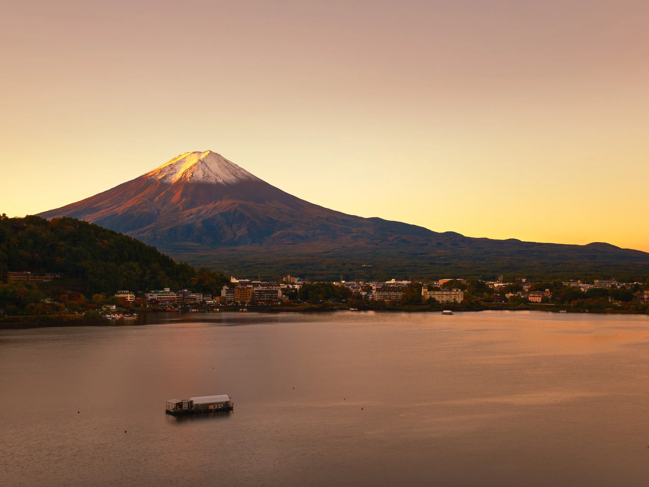Mount Fuji at sunset with city and lake in the foreground.