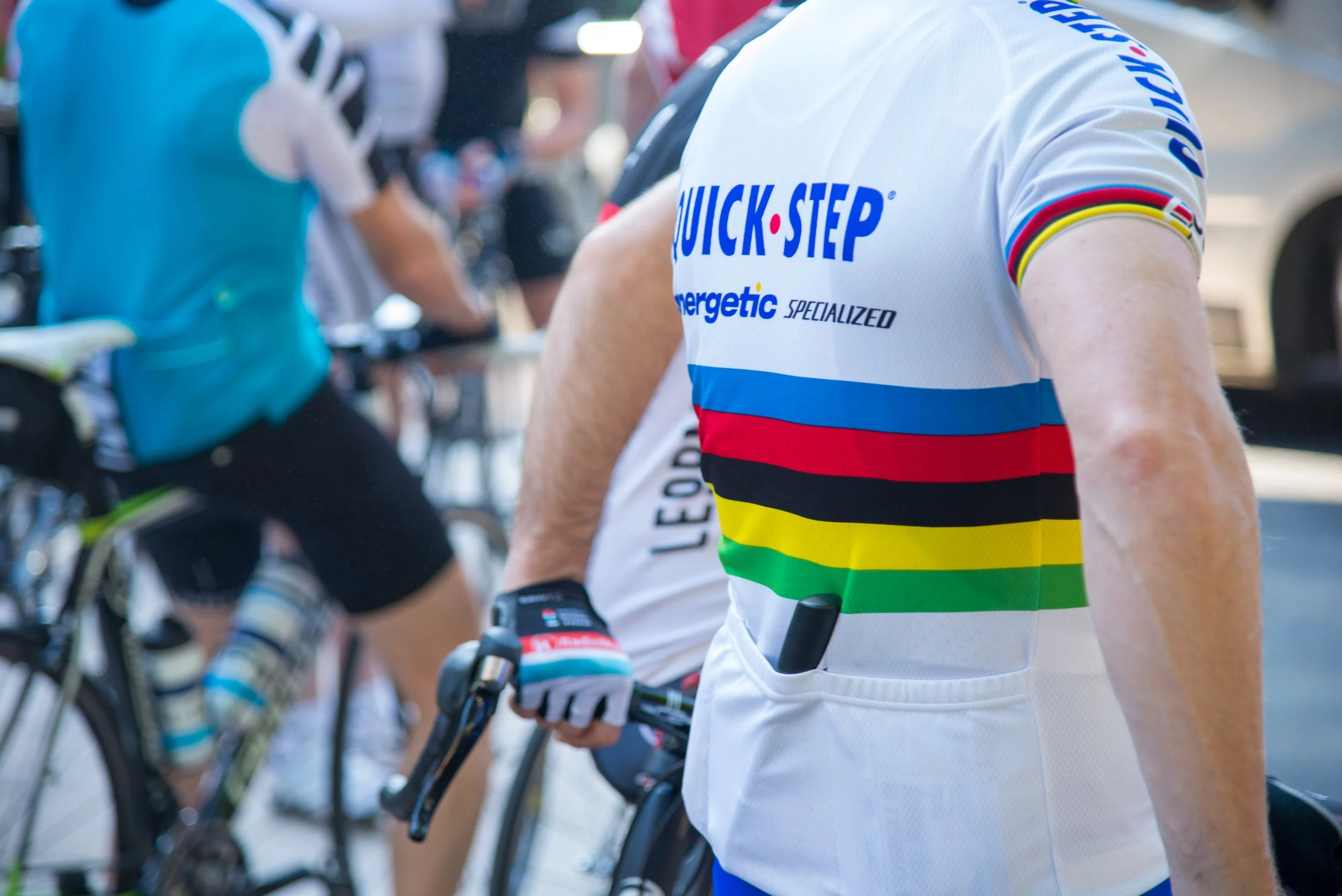 Close-up of a cyclist wearing a colorful jersey with the words 'Quick-Step' on the chest, holding the handlebars of a bike during a race or event.