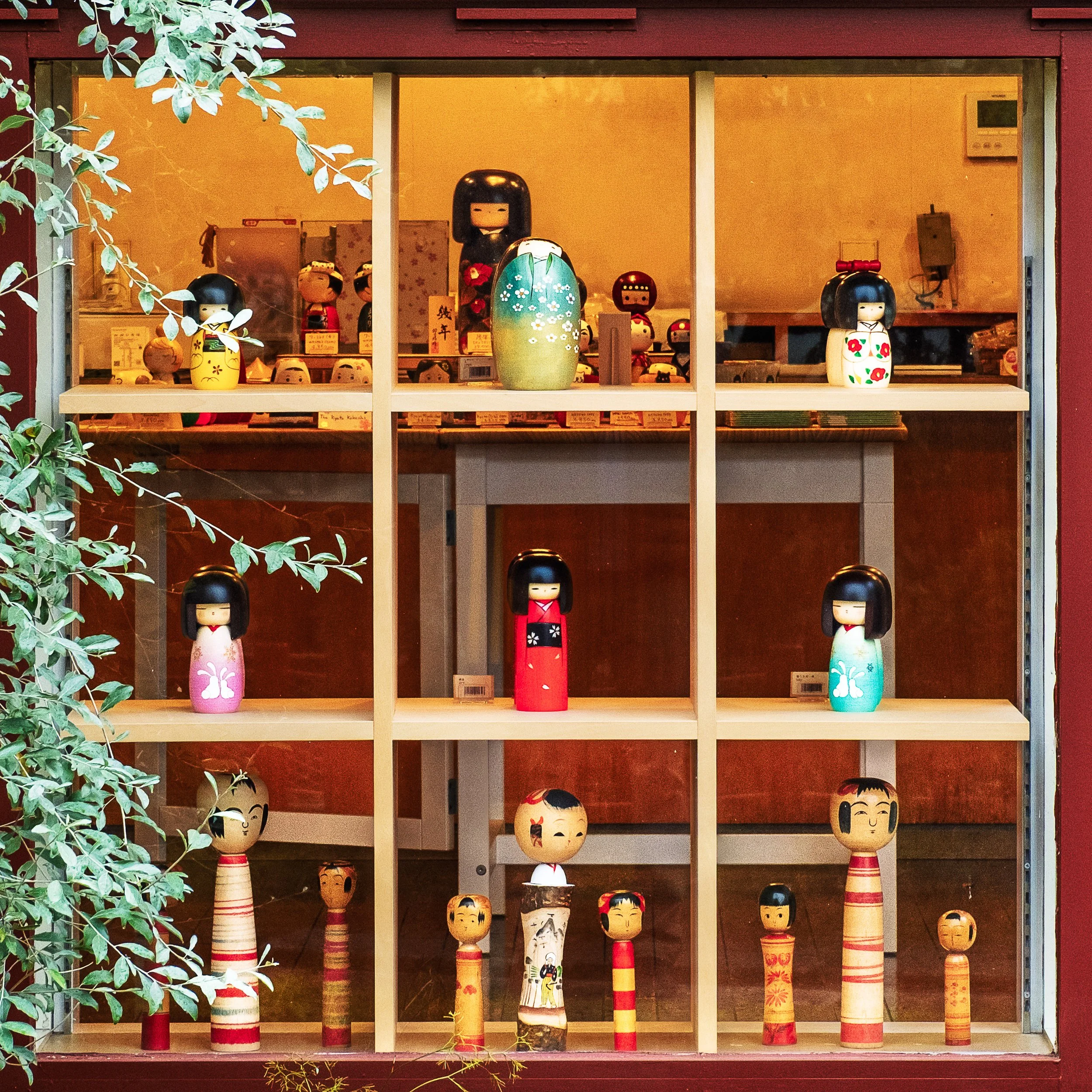 Display of various traditional Japanese Kokeshi dolls arranged on shelves in a shop window.