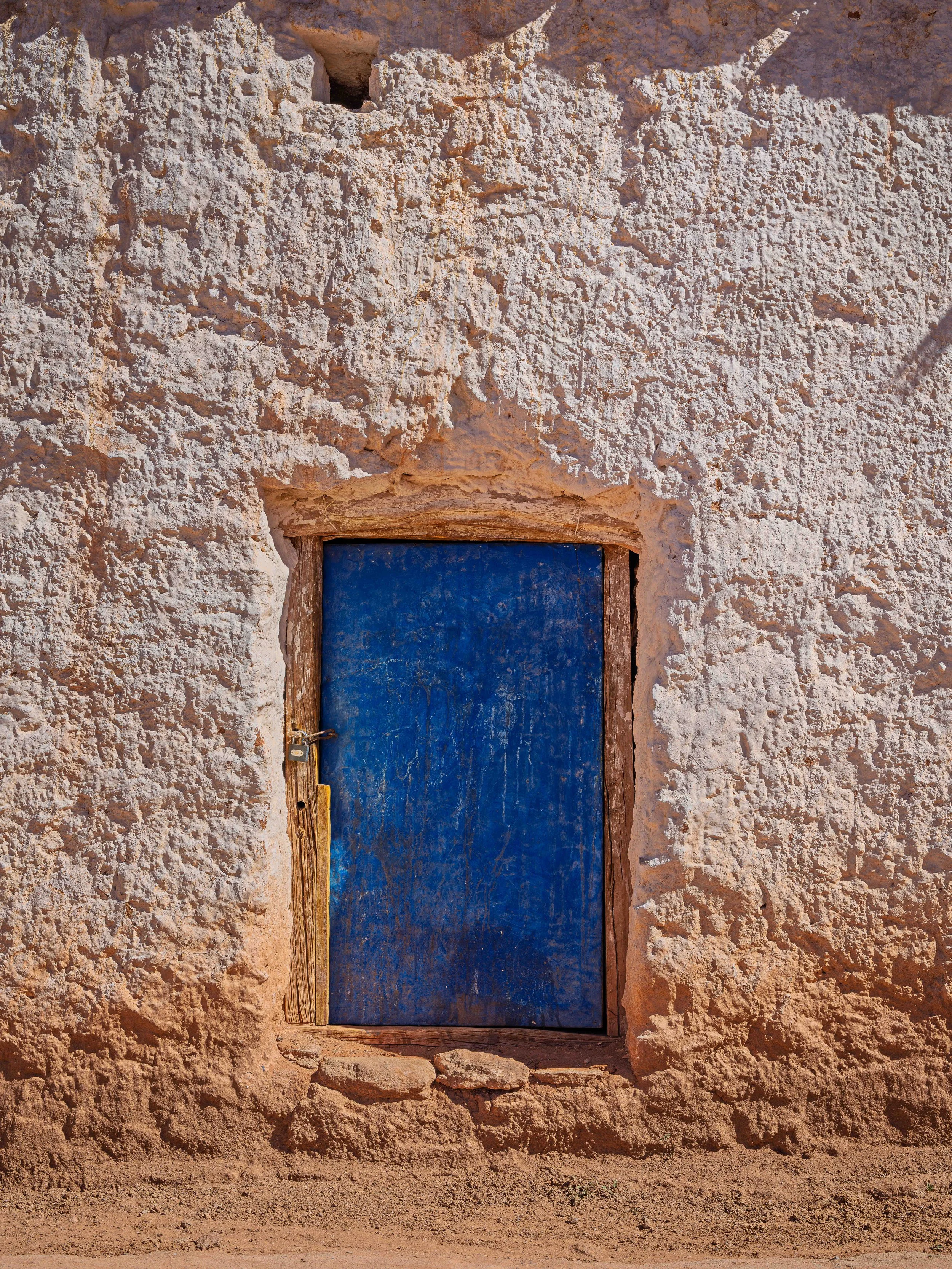 A small, rustic blue door set into a textured, beige stone wall.