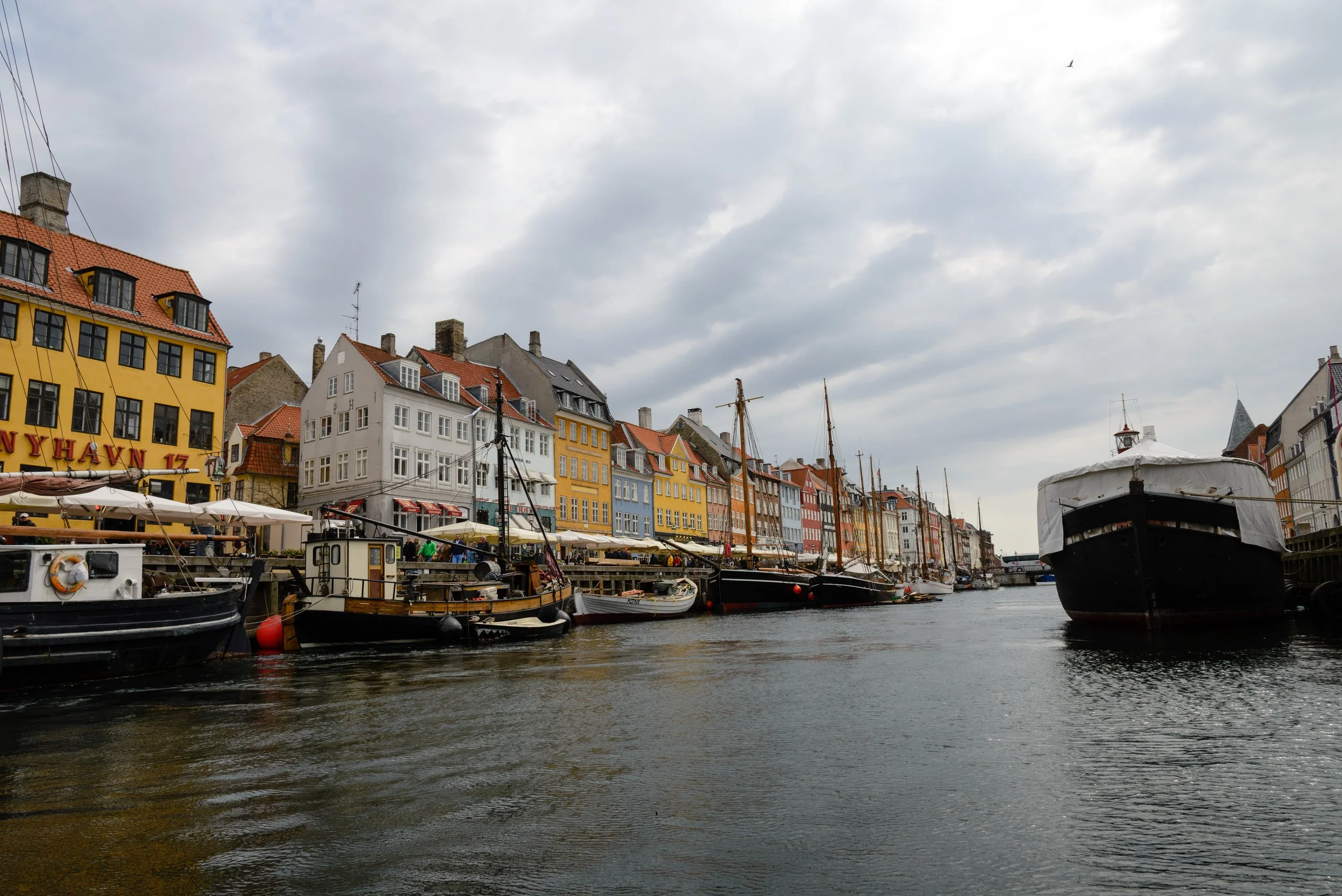 Colorful buildings along a canal with boats docked in Copenhagen, Denmark under cloudy skies.