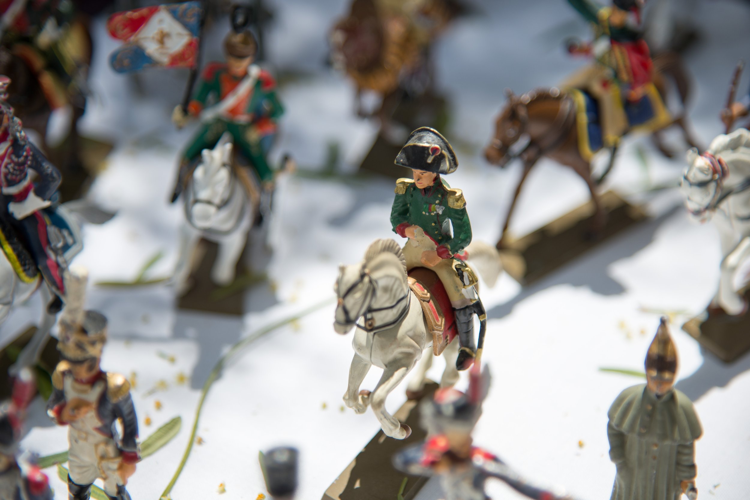 Miniature figurines of soldiers on horseback, dressed in historical military uniforms, arranged on a surface with some snow.