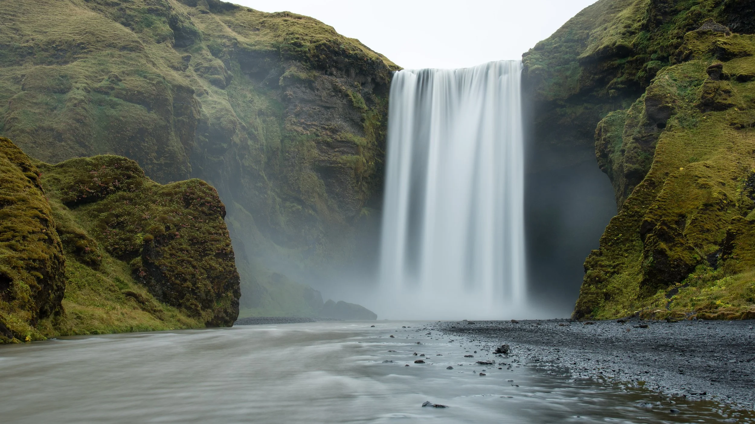 A large waterfall cascading over moss-covered cliffs into a river below