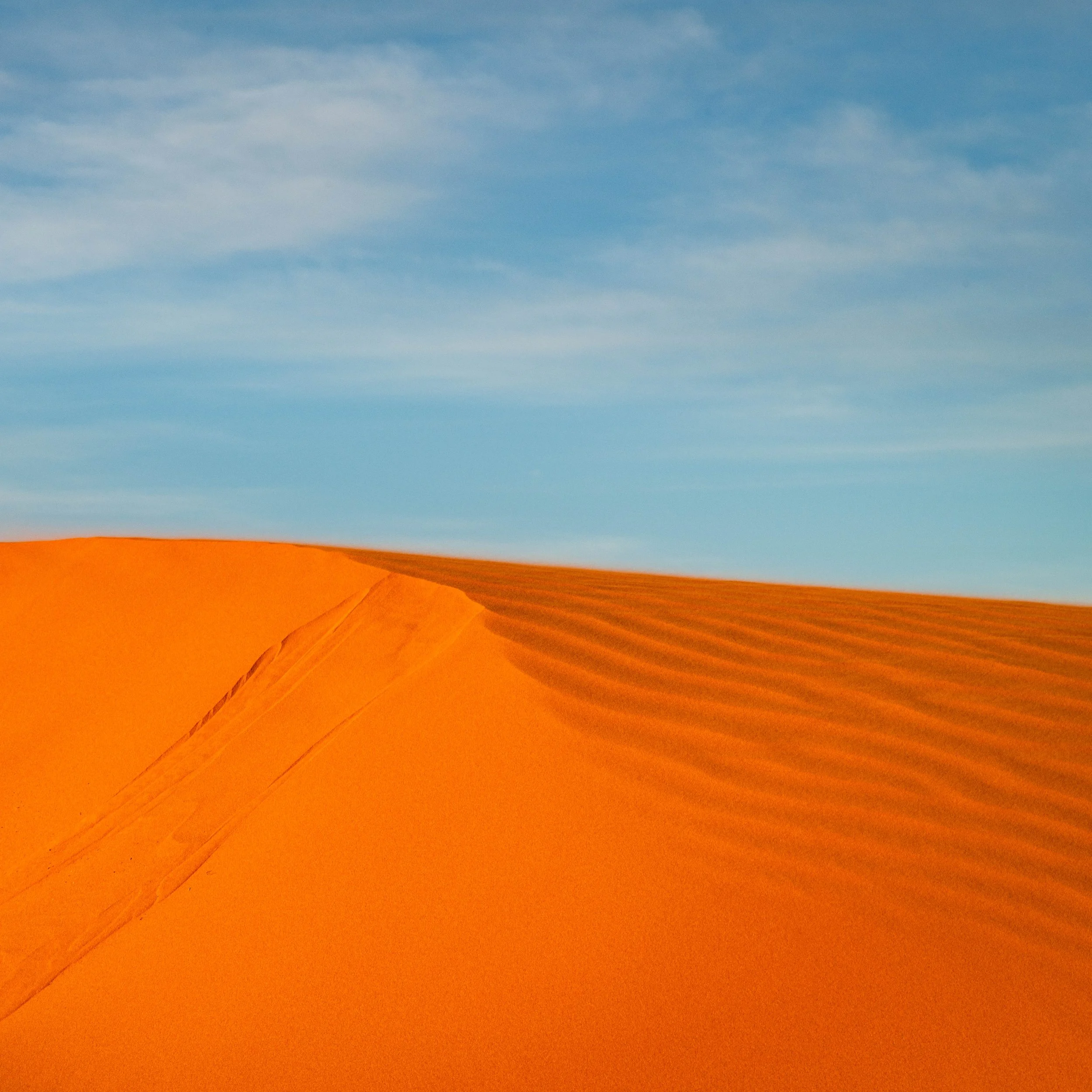 Sand dunes in a desert with a blue sky and some clouds.