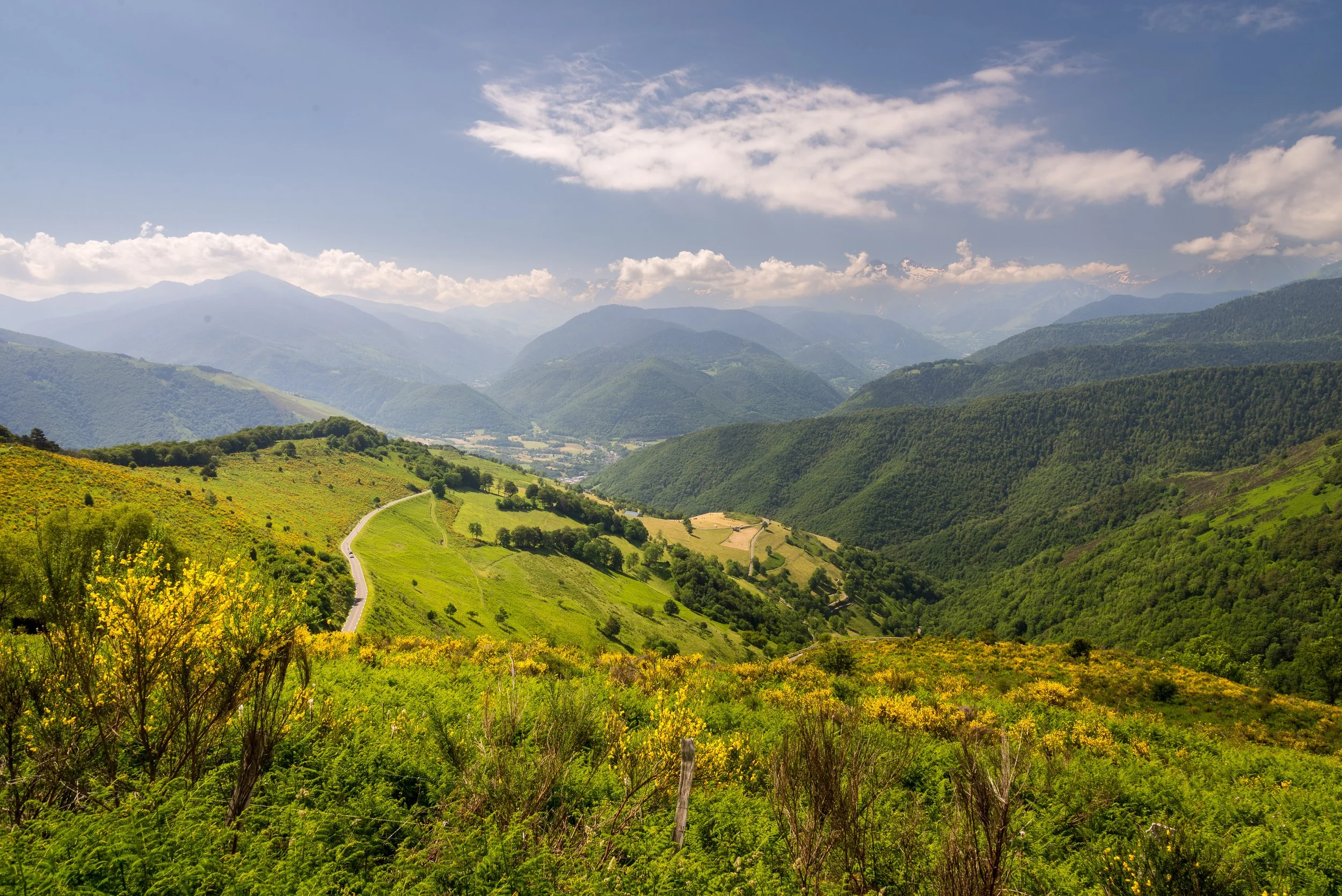 Scenic view of green rolling hills and mountains under a partly cloudy sky with a winding road through the valley.