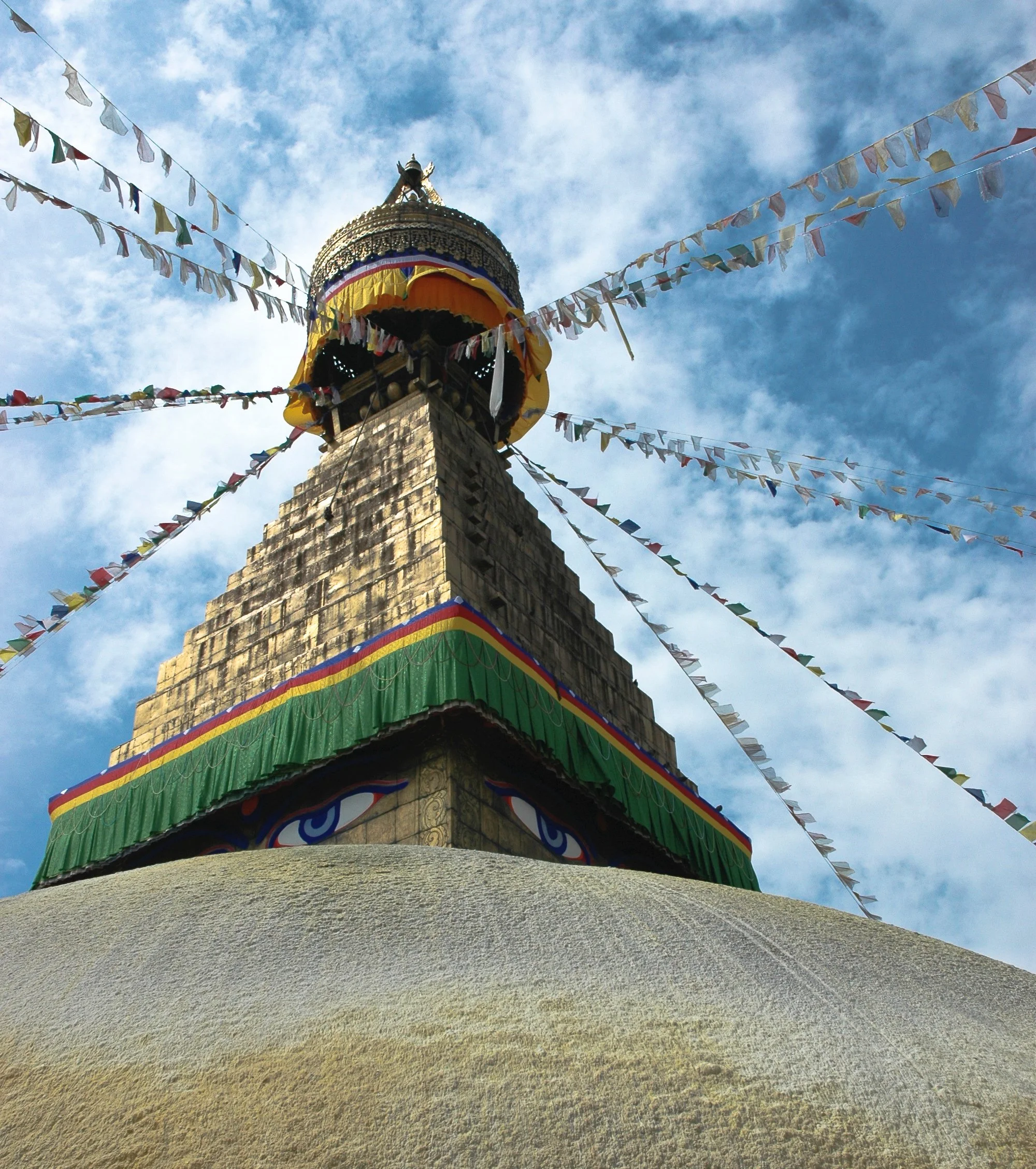 Close-up of a Buddhist stupa with colorful prayer flags, against a blue sky with clouds.
