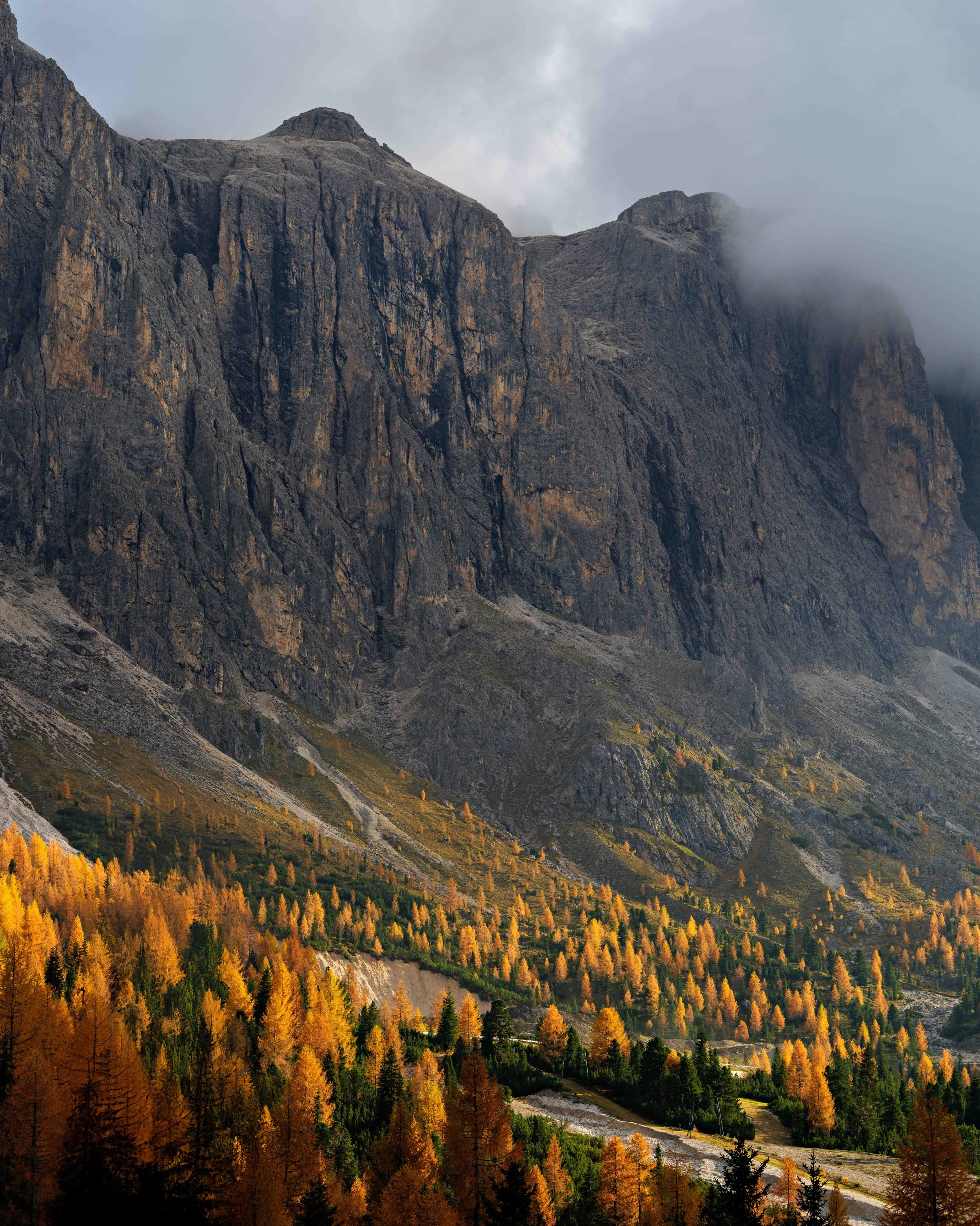 A mountain with steep rocky cliffs partially covered by low clouds, and a forested slope in autumn colors at the base.