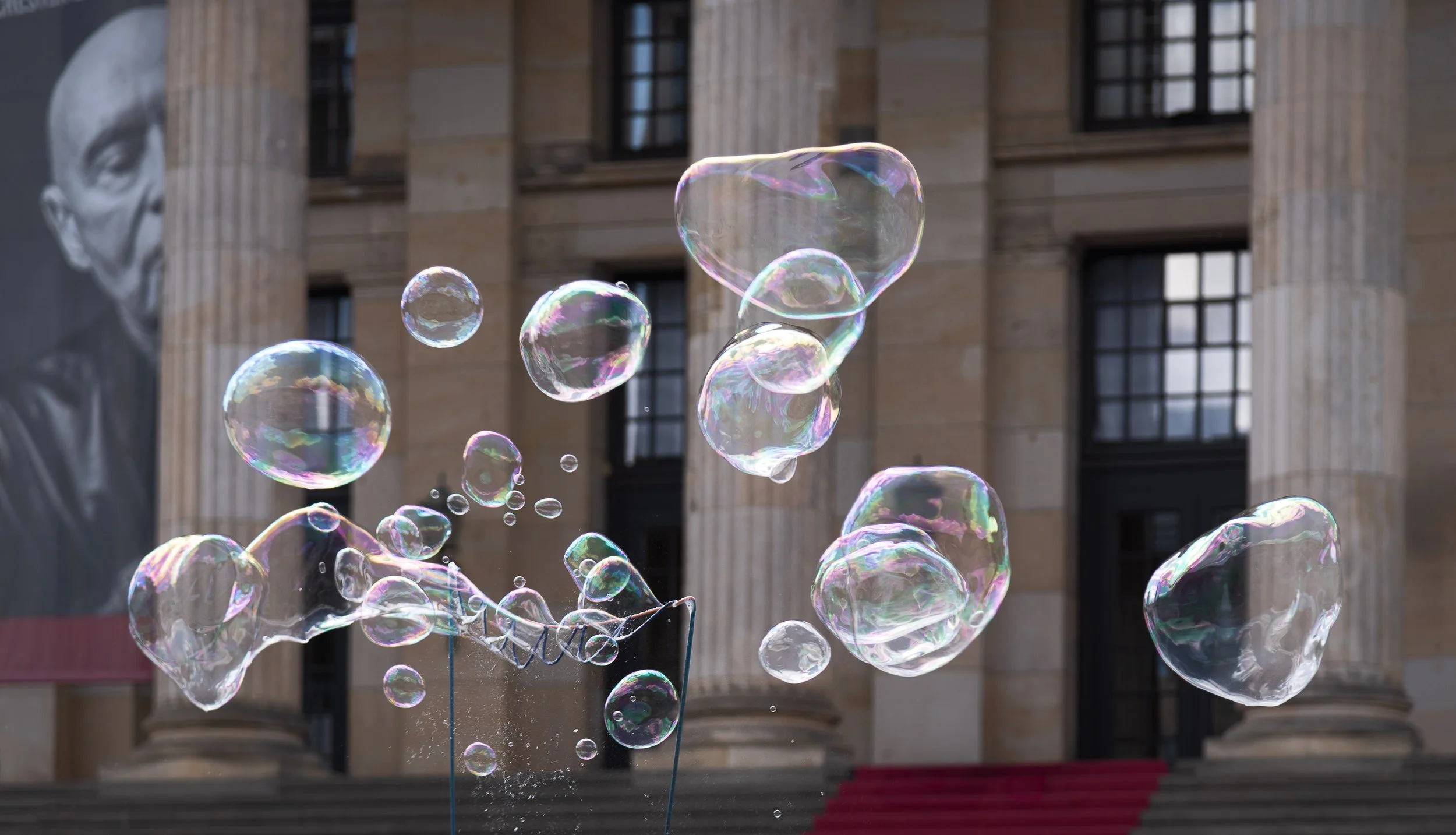 Soap bubbles floating in front of a neoclassical building with columns and large windows.