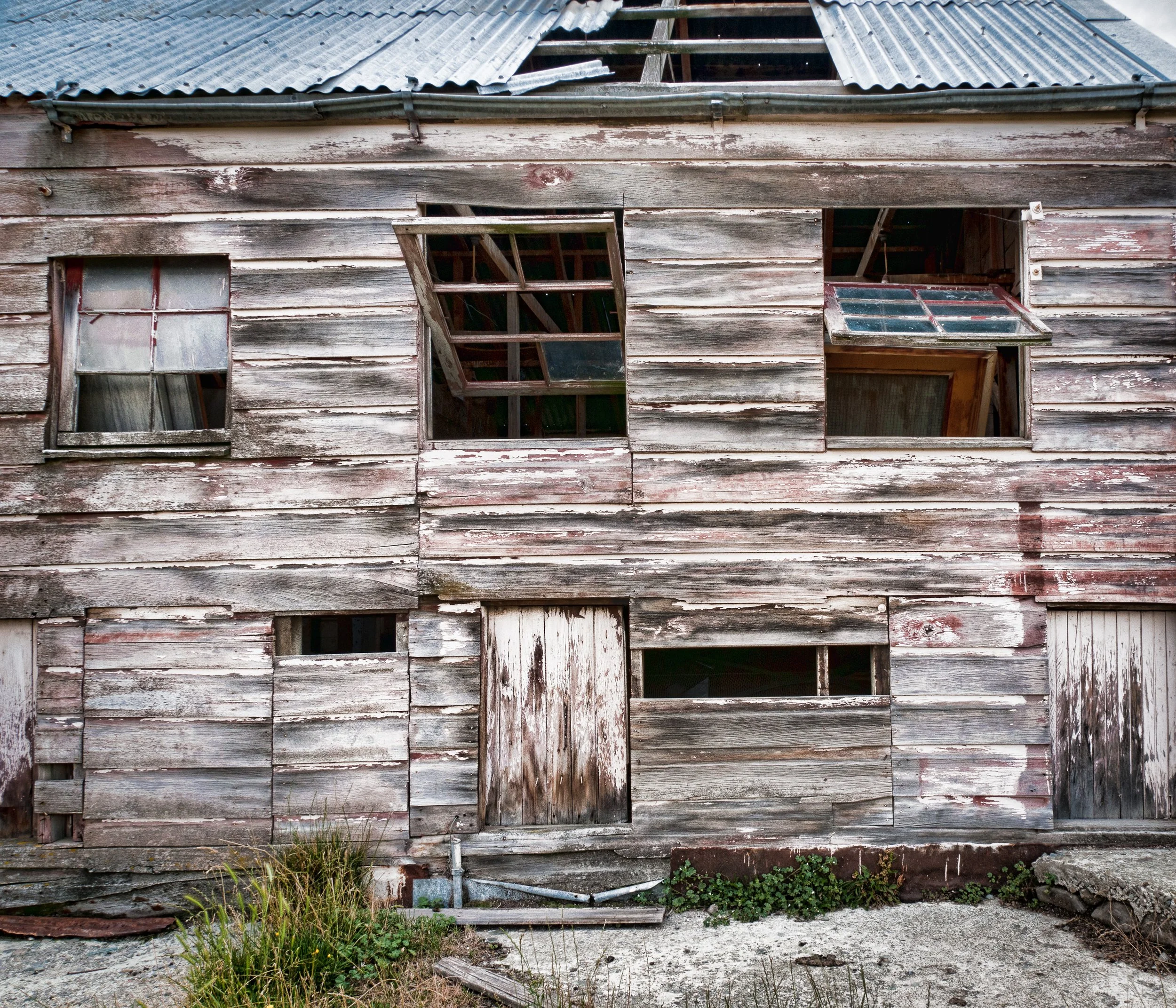 An old, dilapidated wooden house with peeling paint, broken windows, and a damaged metal roof.