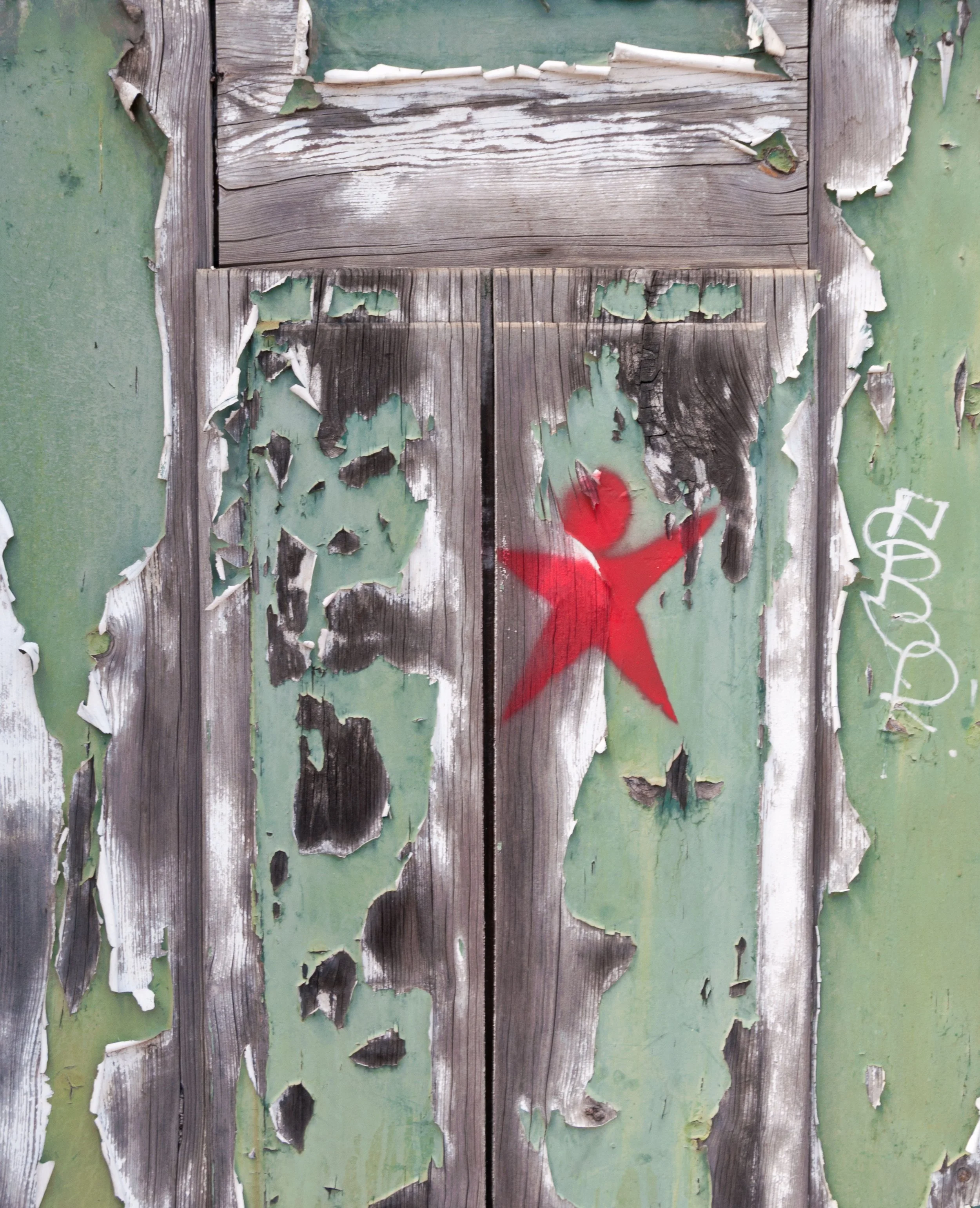 Old, weathered wooden door with peeling green paint and graffiti, including a red star and white writing.