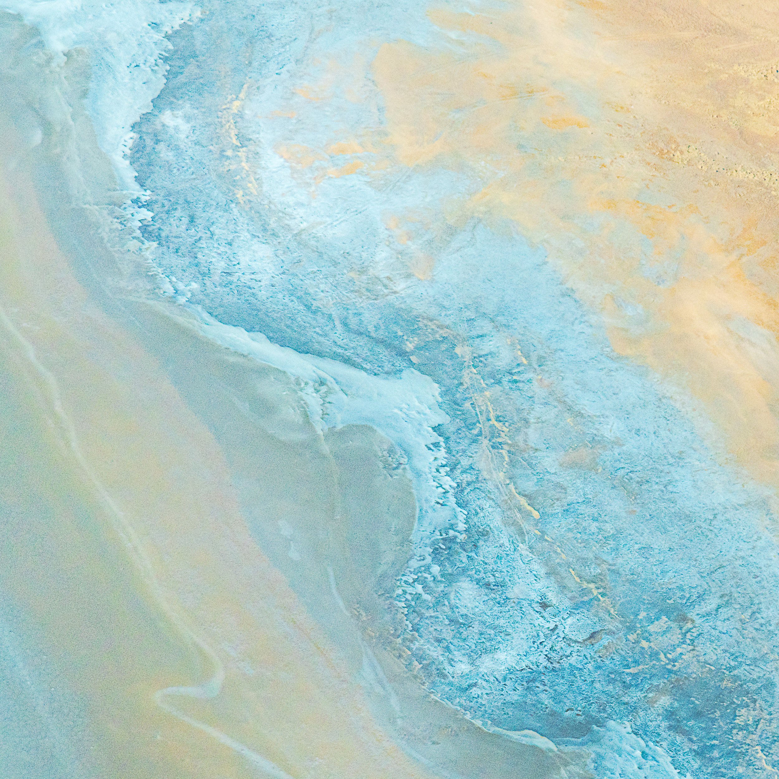 Abstract aerial view of a icy landscape with shades of blue, white, and beige, resembling a frozen lake or salt flat.