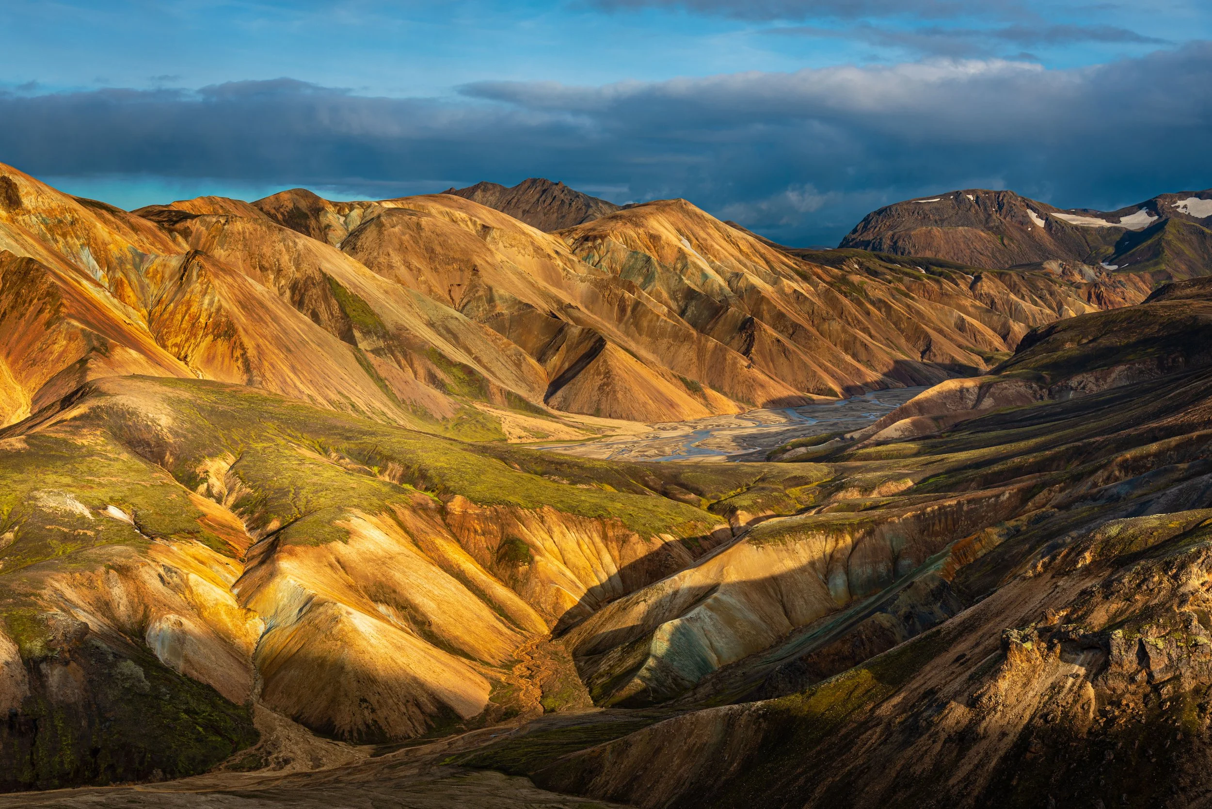 Colorful mountain range with multicolored layers, a river running through the valley, and clouds in the sky.