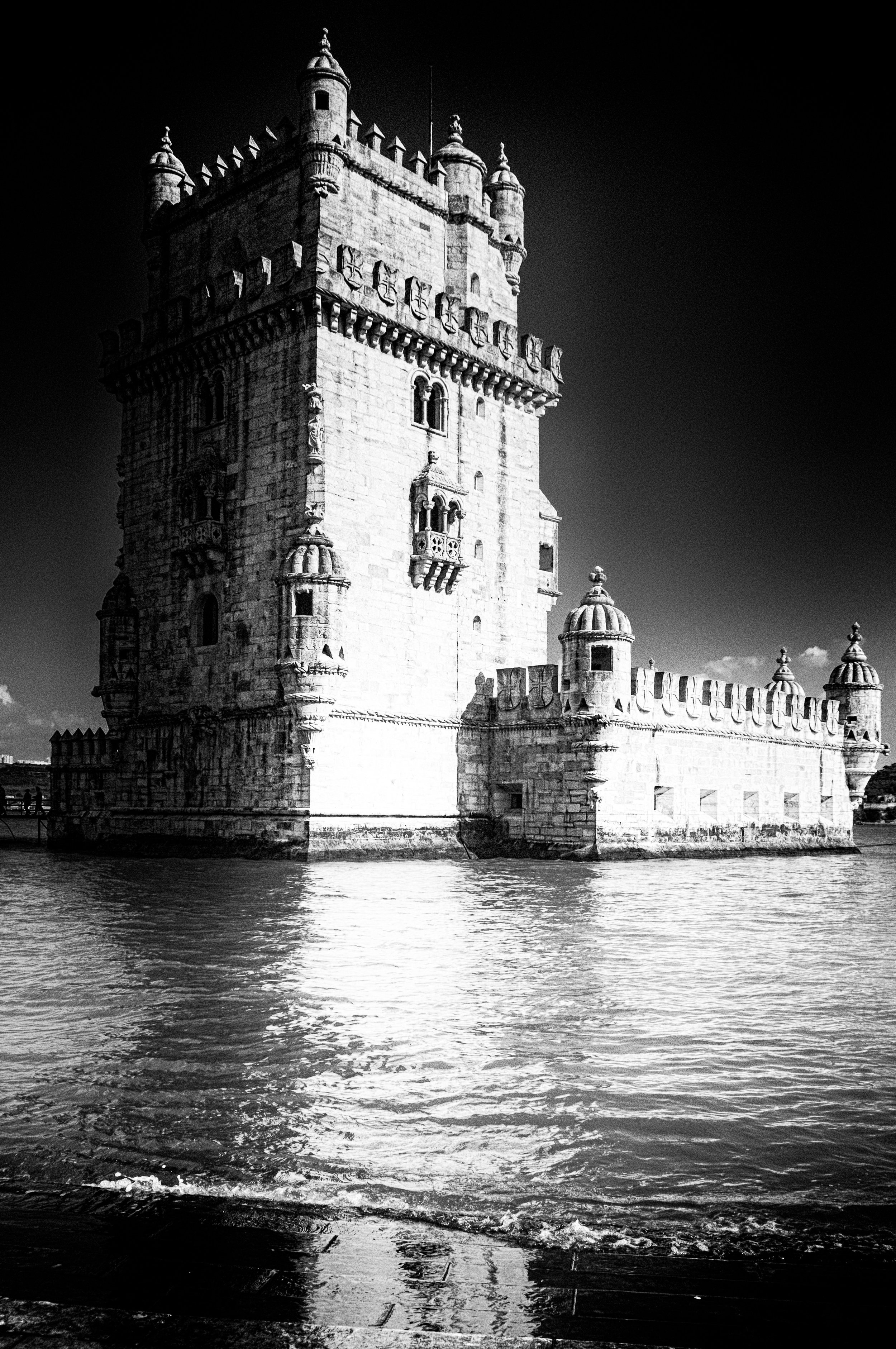 Black and white photo of a historic castle surrounded by water, with a clear sky in the background.