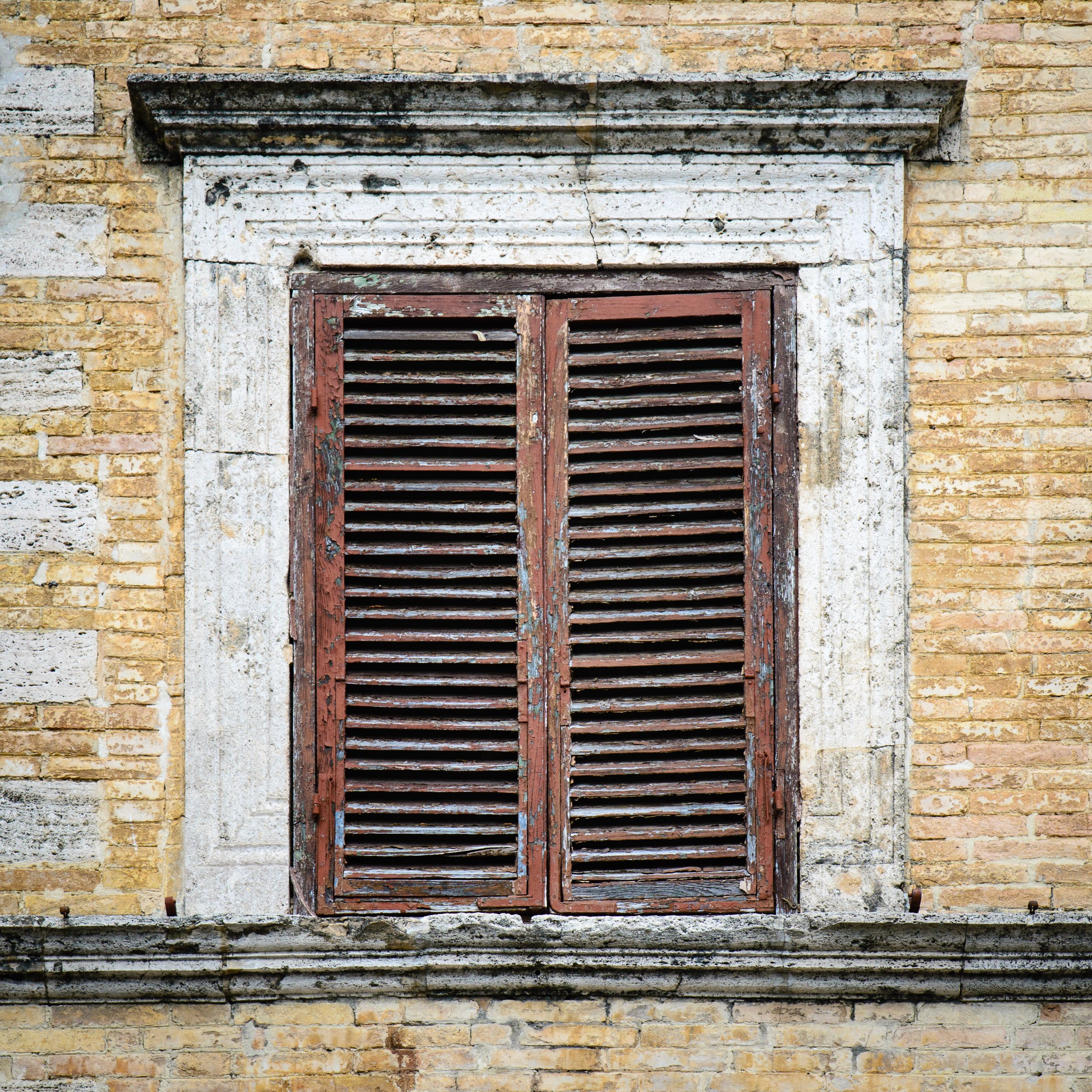 Old wooden window shutters on a brick building with weathered paint and stone trim.