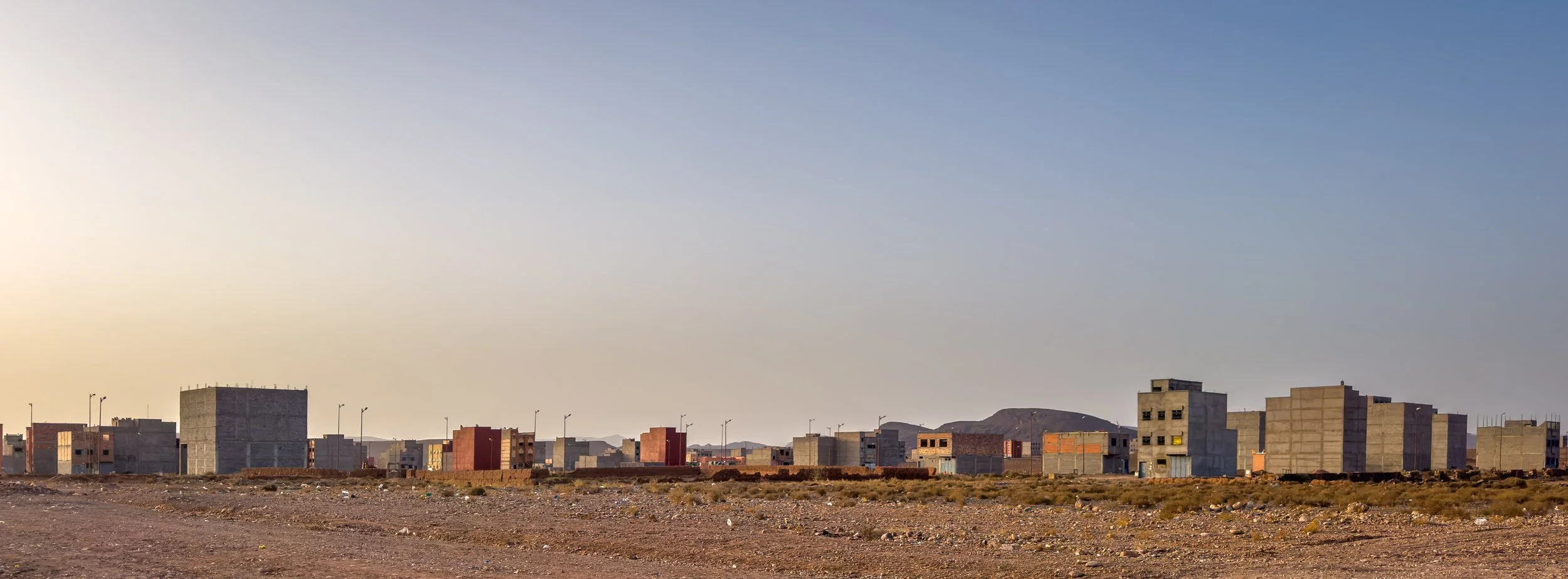 A row of unfinished concrete buildings in a desert landscape under a clear blue sky.