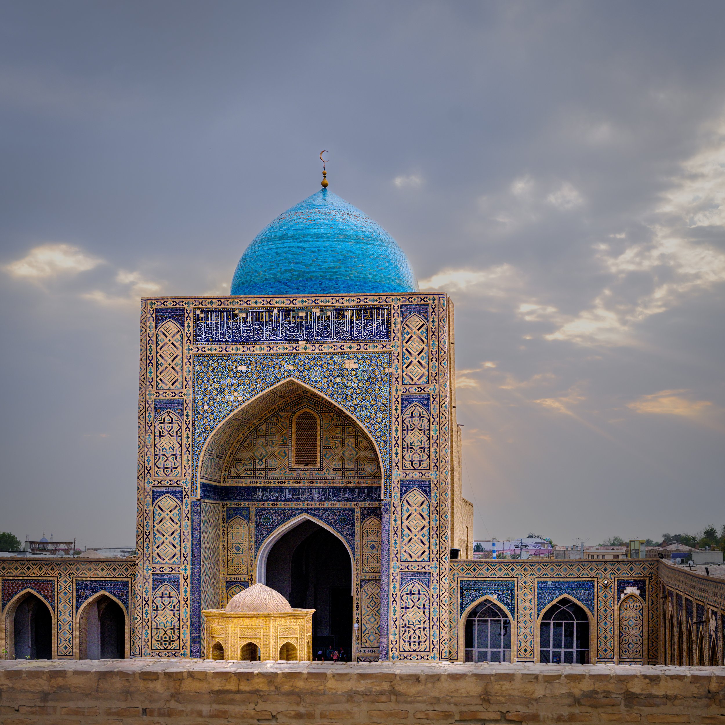 View of a mosque with intricate tile work and blue dome under a cloudy sky at sunset.