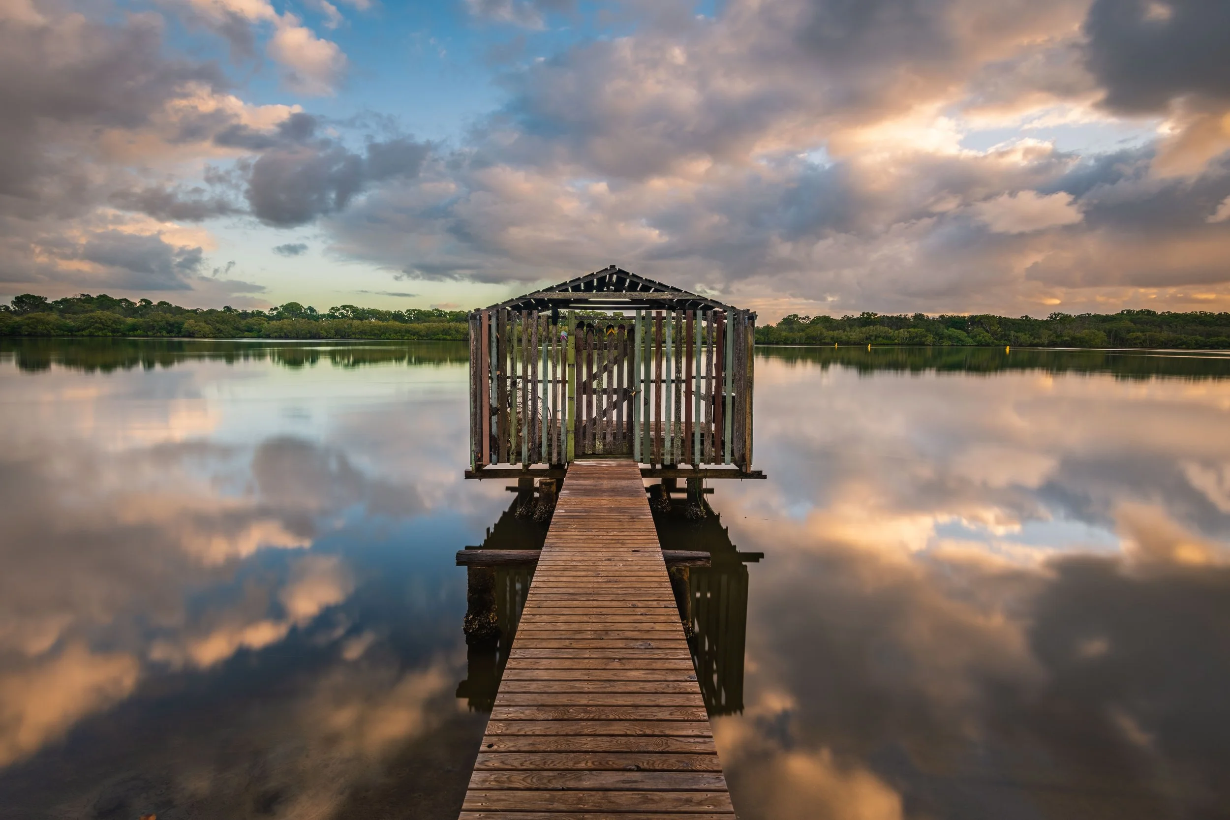 Long exposure sunrise of quirky colorful fishing shack and jetty with reflections on smooth waters of Maroochy River | Brisbane landscape and travel photographer Ralph McConaghy