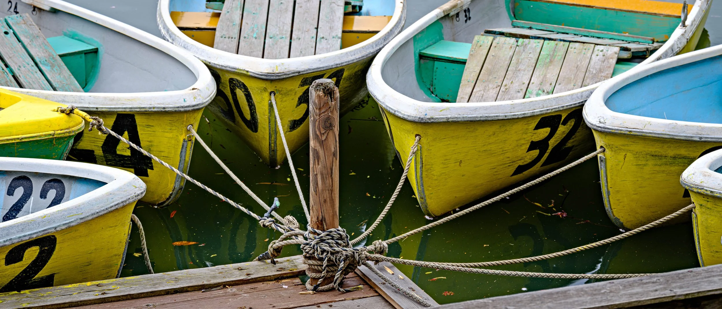 Colorful small boats docked at a pier, tied to a wooden post with ropes, with visible boat numbers and weathered wood.