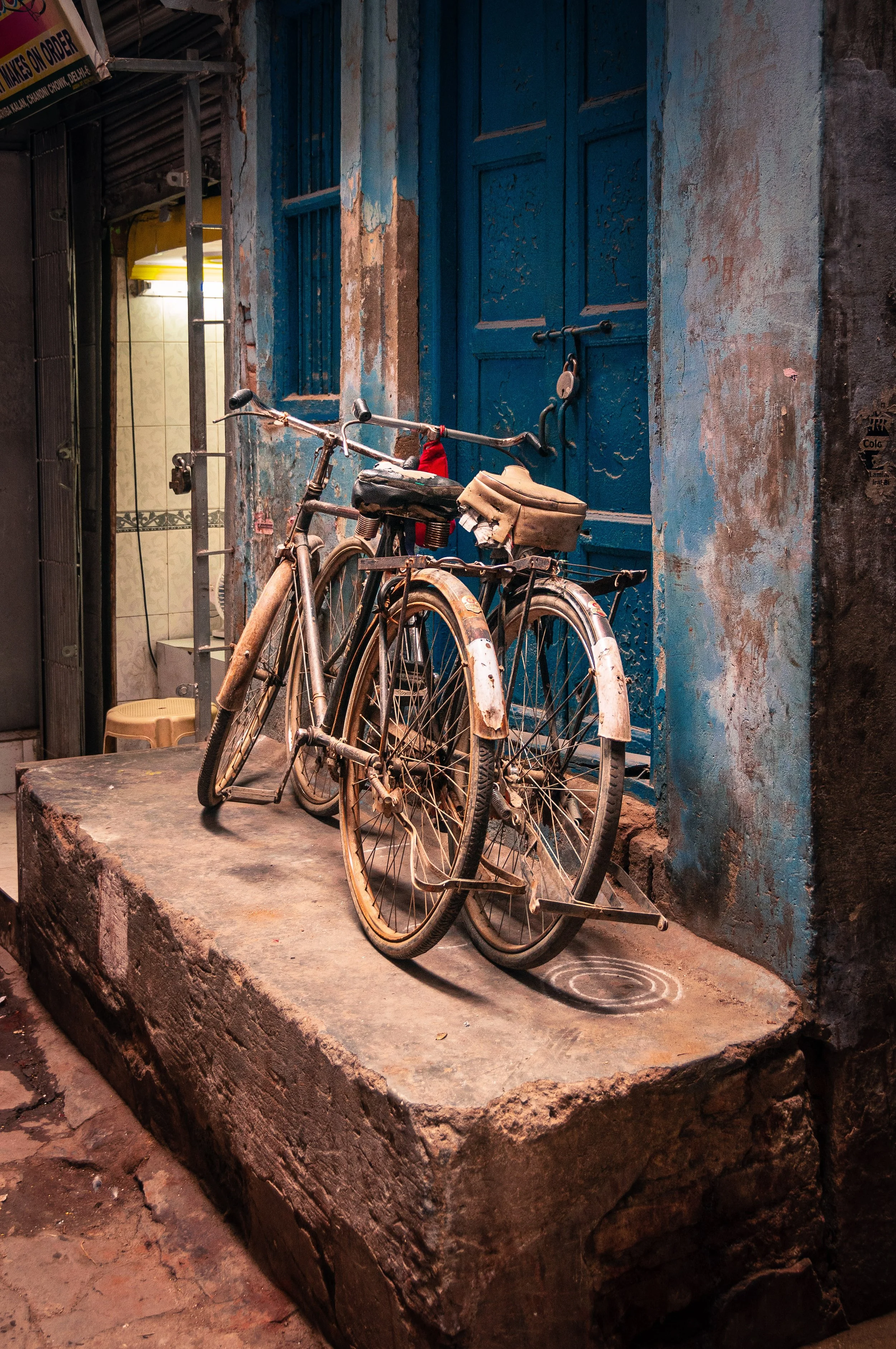 Two old rusted bicycles parked in front of a weathered blue door on a stone step.