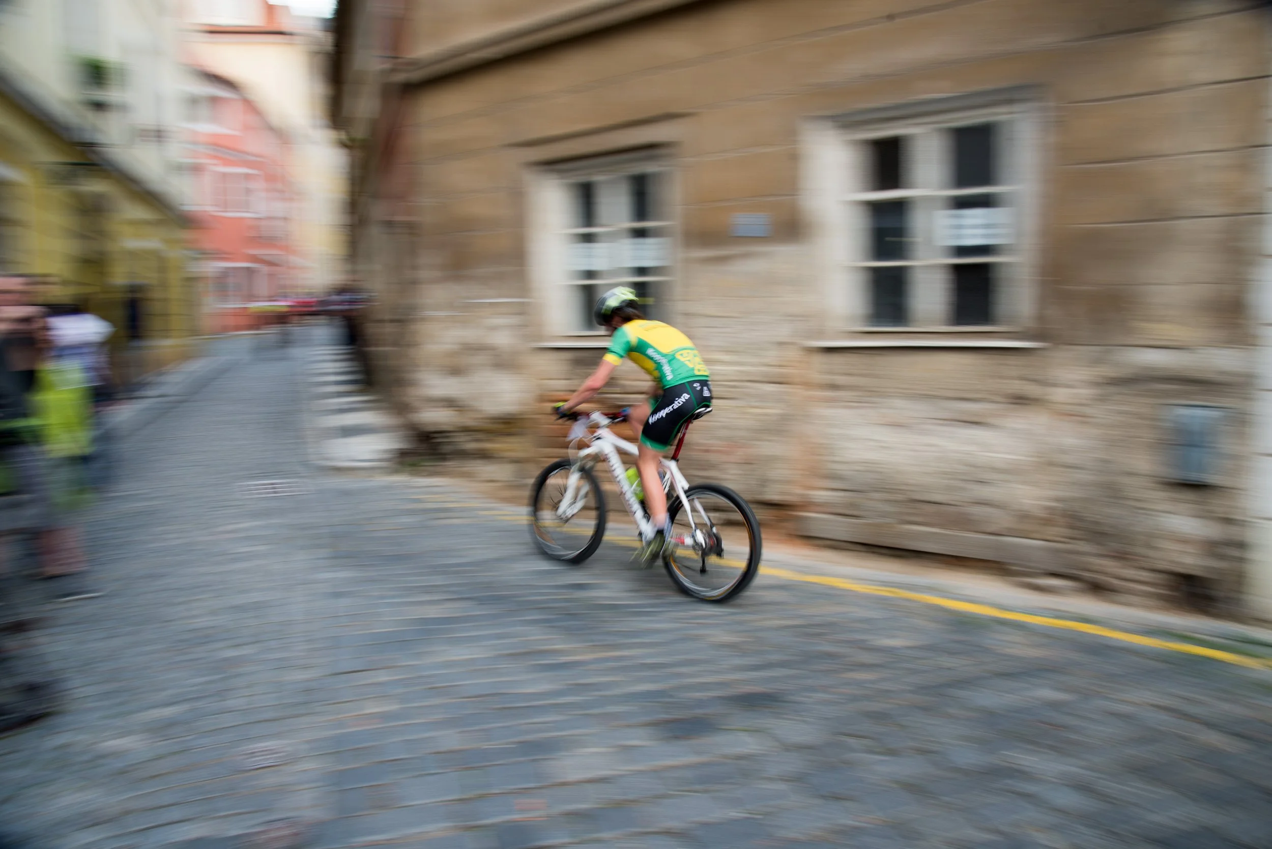 Cyclist riding on cobblestone street with blurred background of buildings.