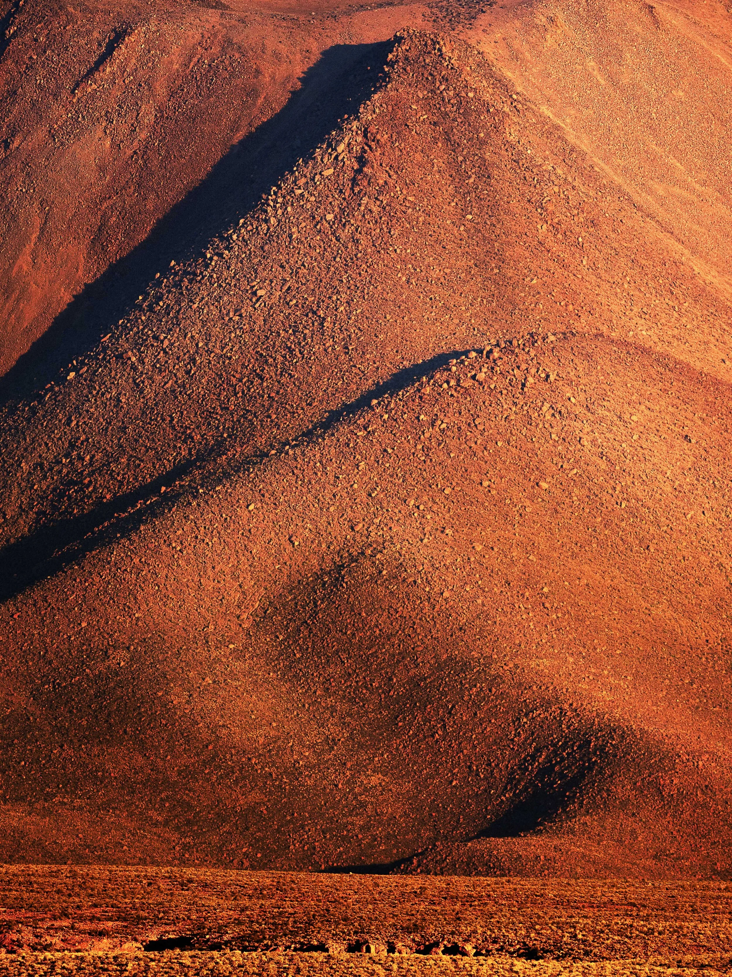 A desert landscape with rolling sand dunes and deep shadows.