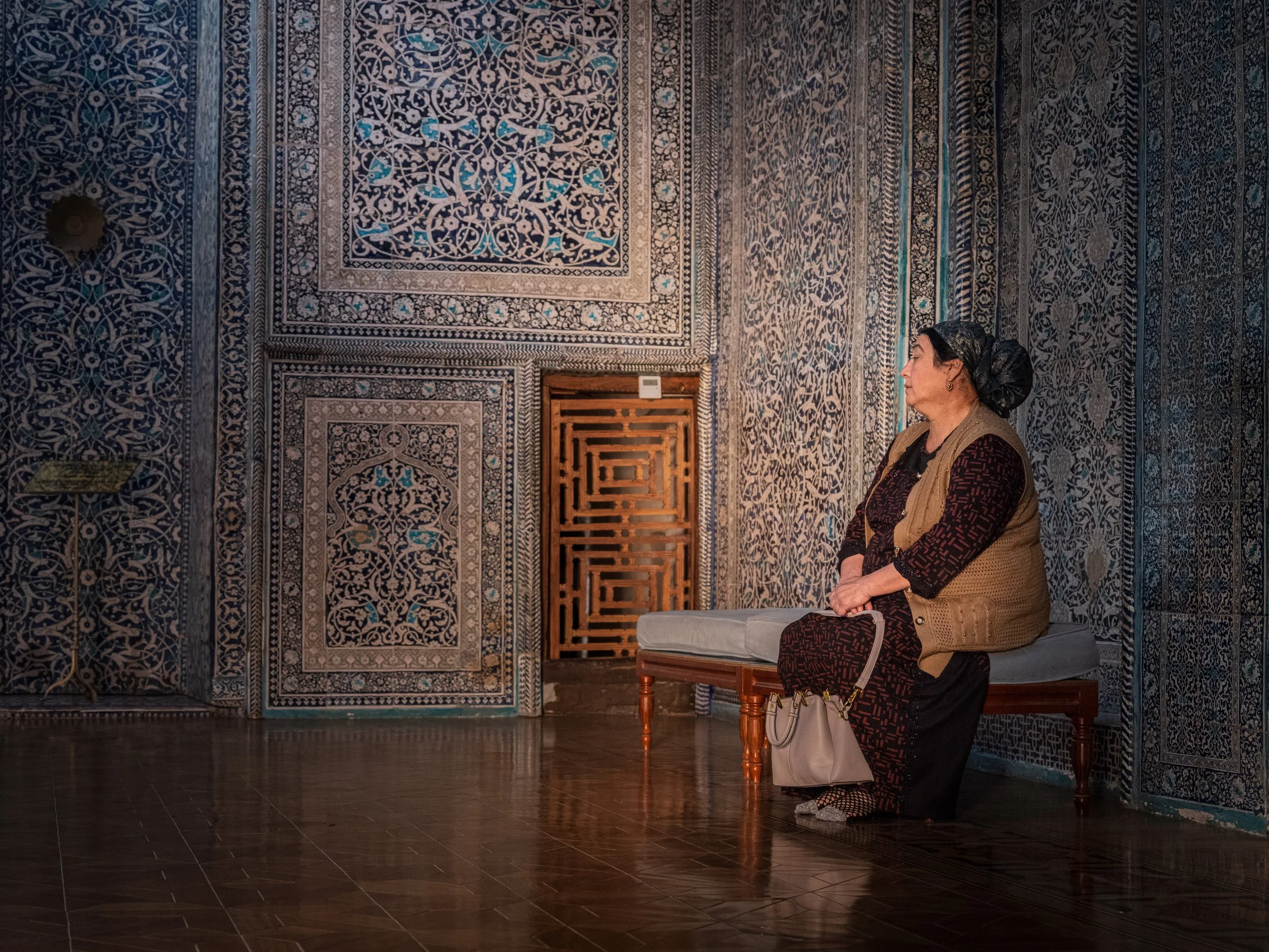 A woman sitting on a bench inside a room with intricately patterned blue and white tiled walls.