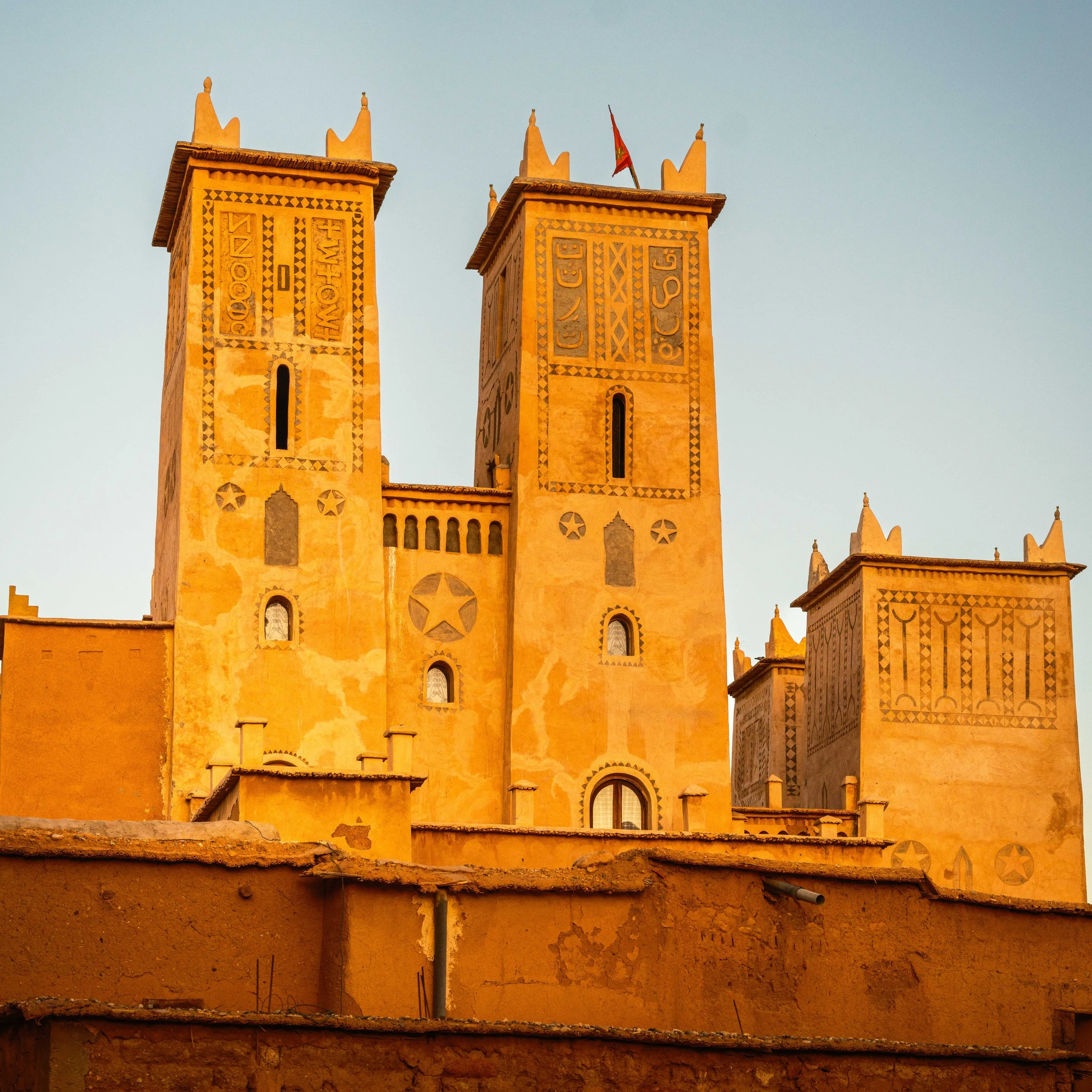 Tall, orange, sandstone buildings with Moroccan architectural details, including decorative patterns and small arched windows, set against a clear sky.