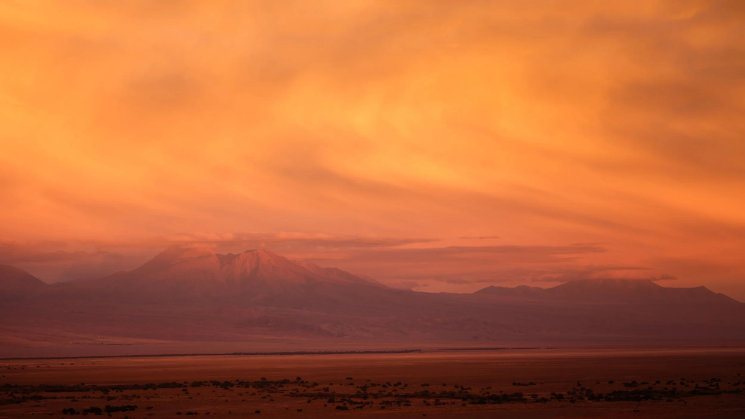 A mountain landscape at sunset with a dramatic sky filled with pink and orange clouds.