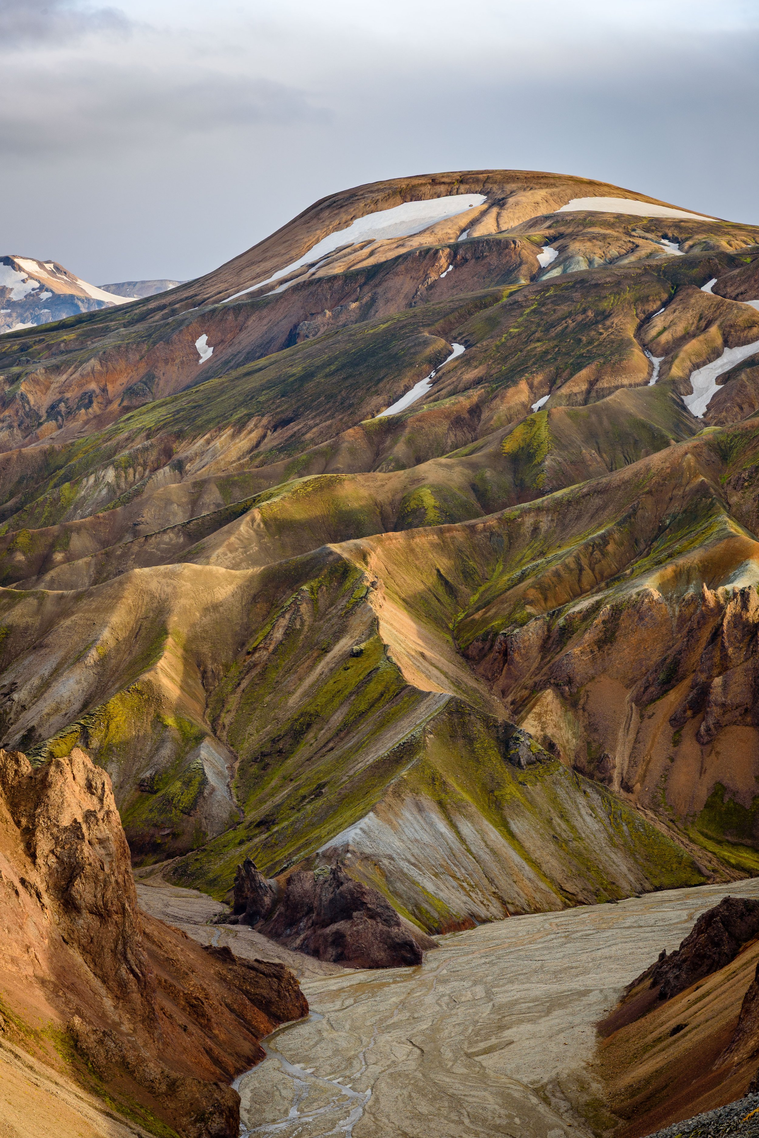 Colorful mountain landscape with patches of snow and a river at the base.
