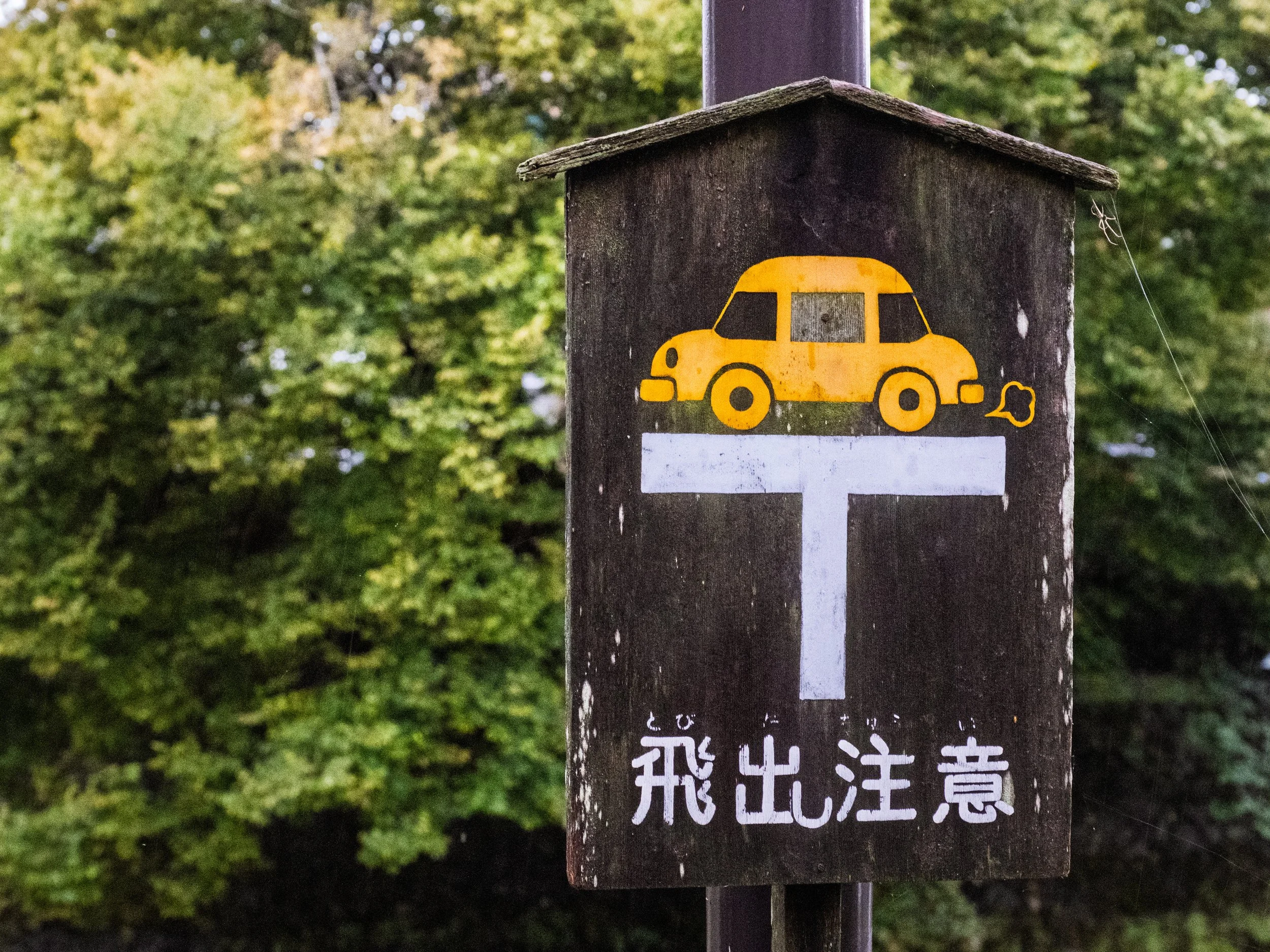 A wooden sign with a yellow car illustration and Japanese text.