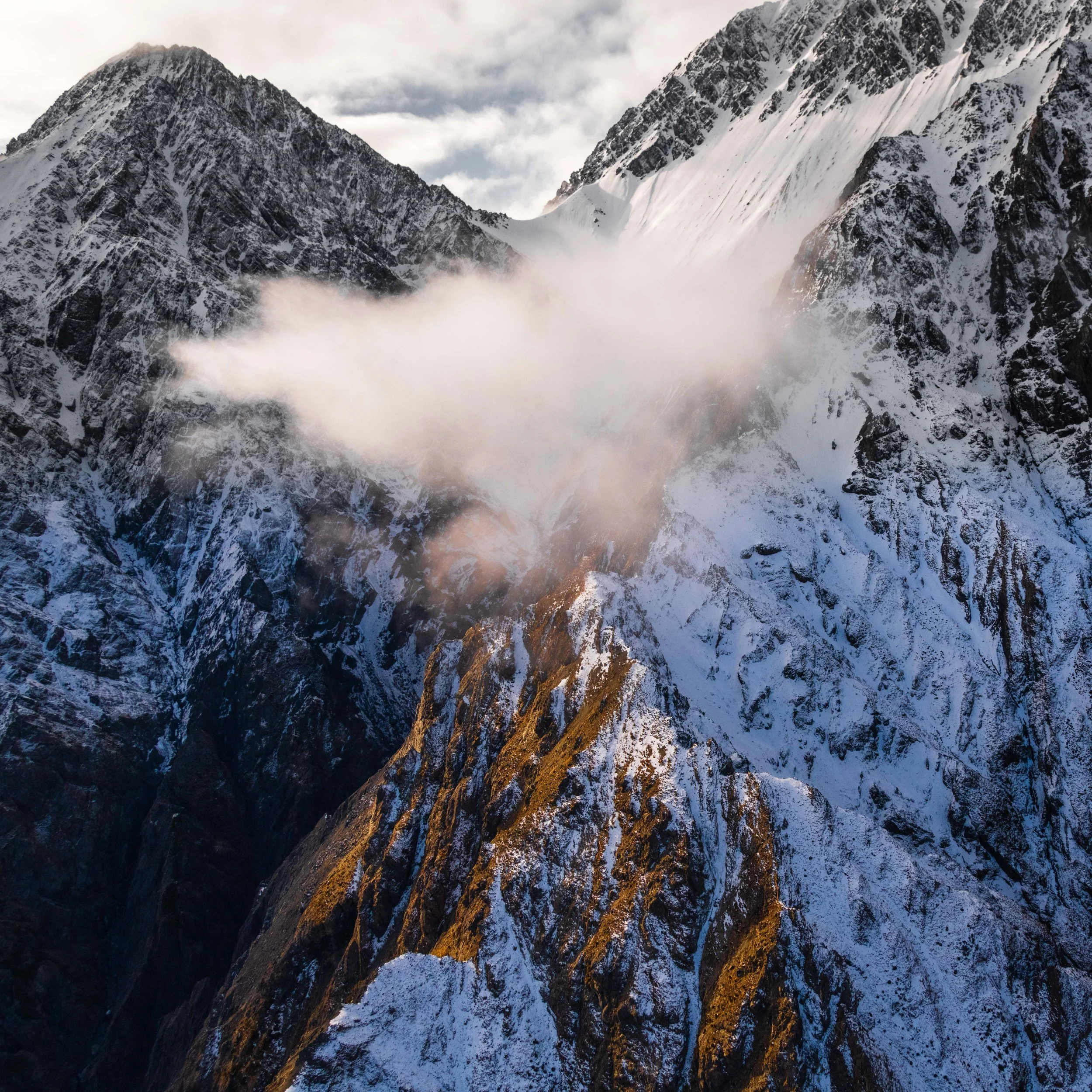 Snow-covered mountain peaks with some clouds and mist in the sky.