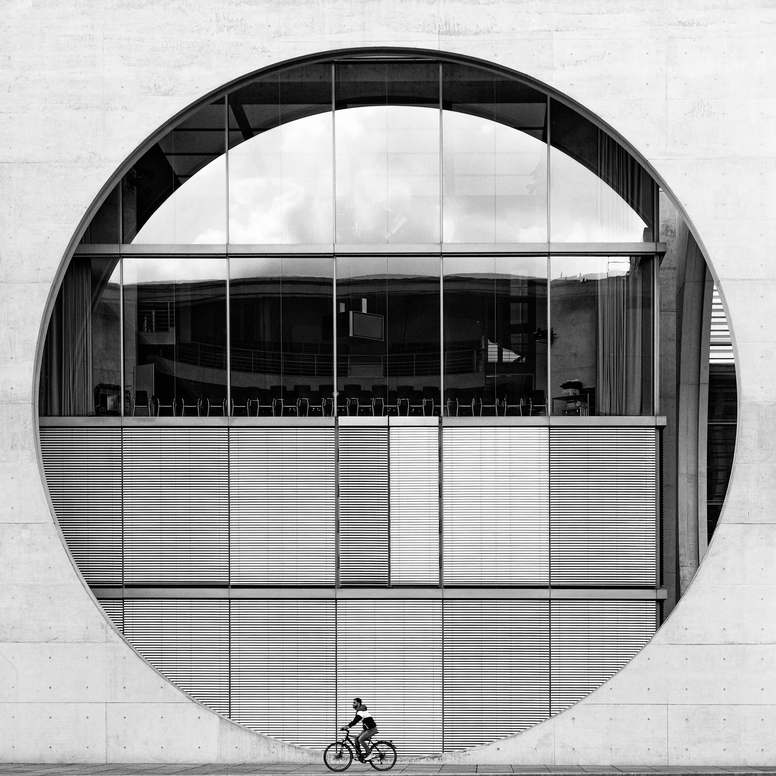 A person riding a bicycle in front of a large round window reflecting a modern building.