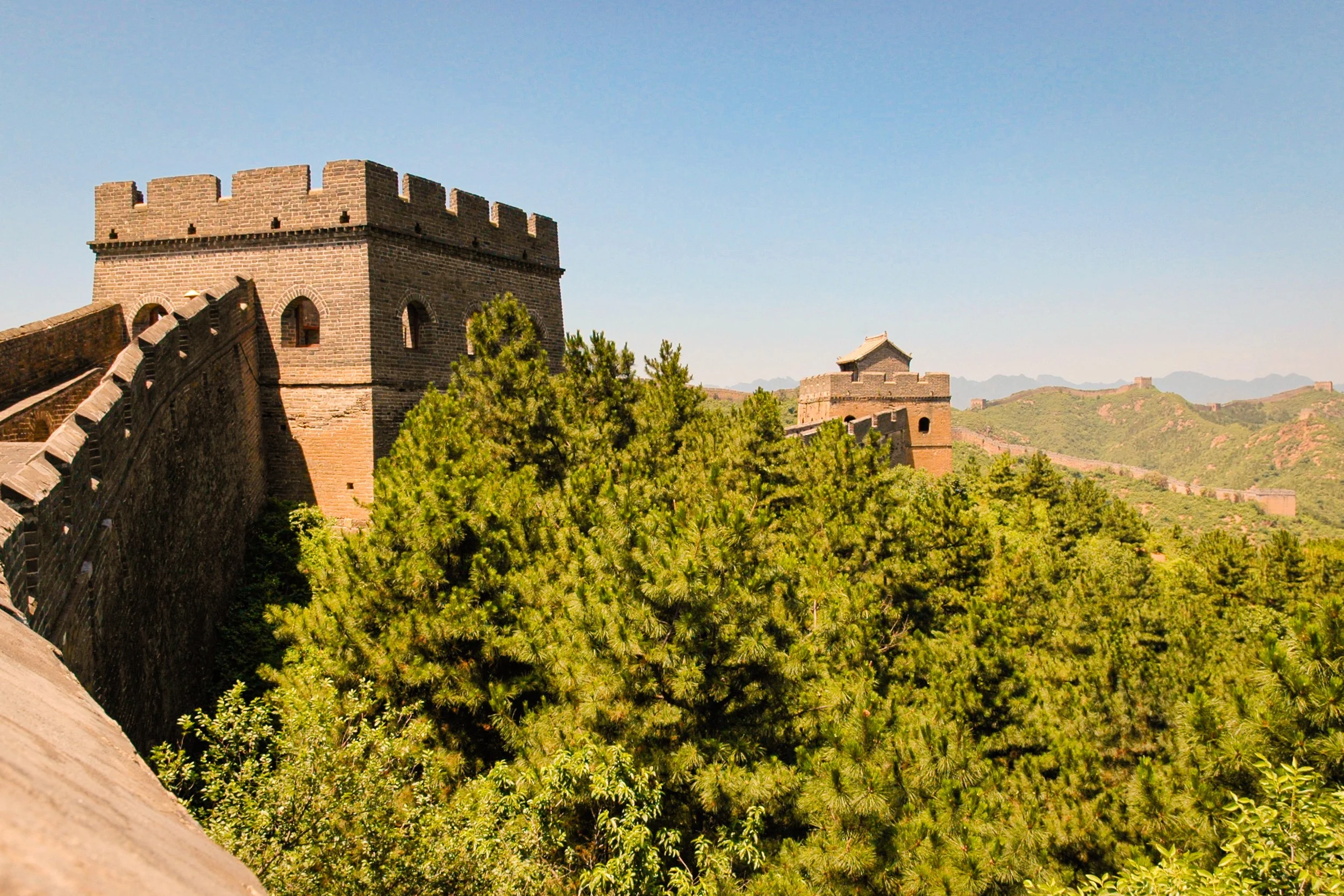 The Great Wall of China stretching through green, hilly landscape under clear blue sky.