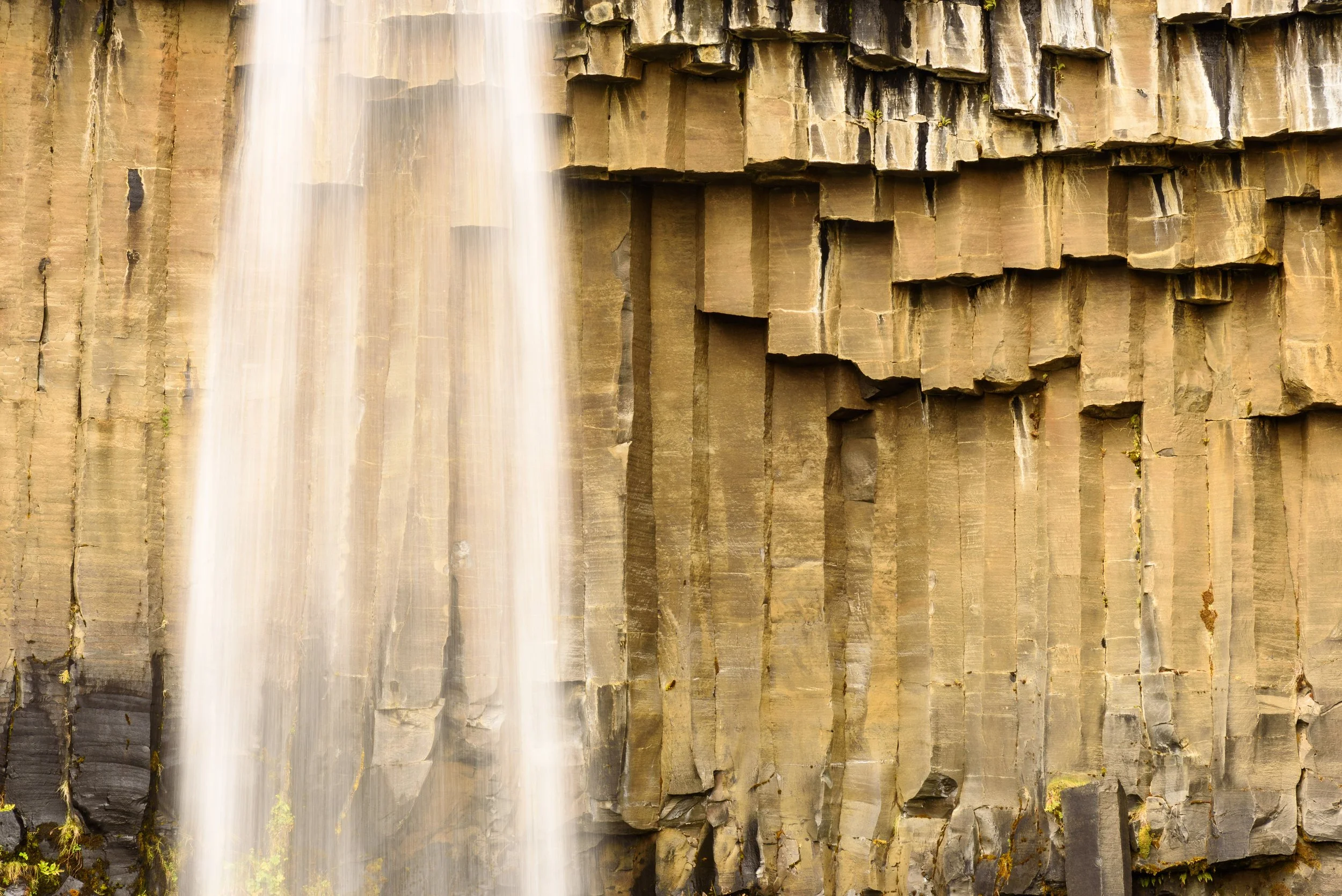 A waterfall flowing down a tall cliffside with hexagonal basalt rock formations.