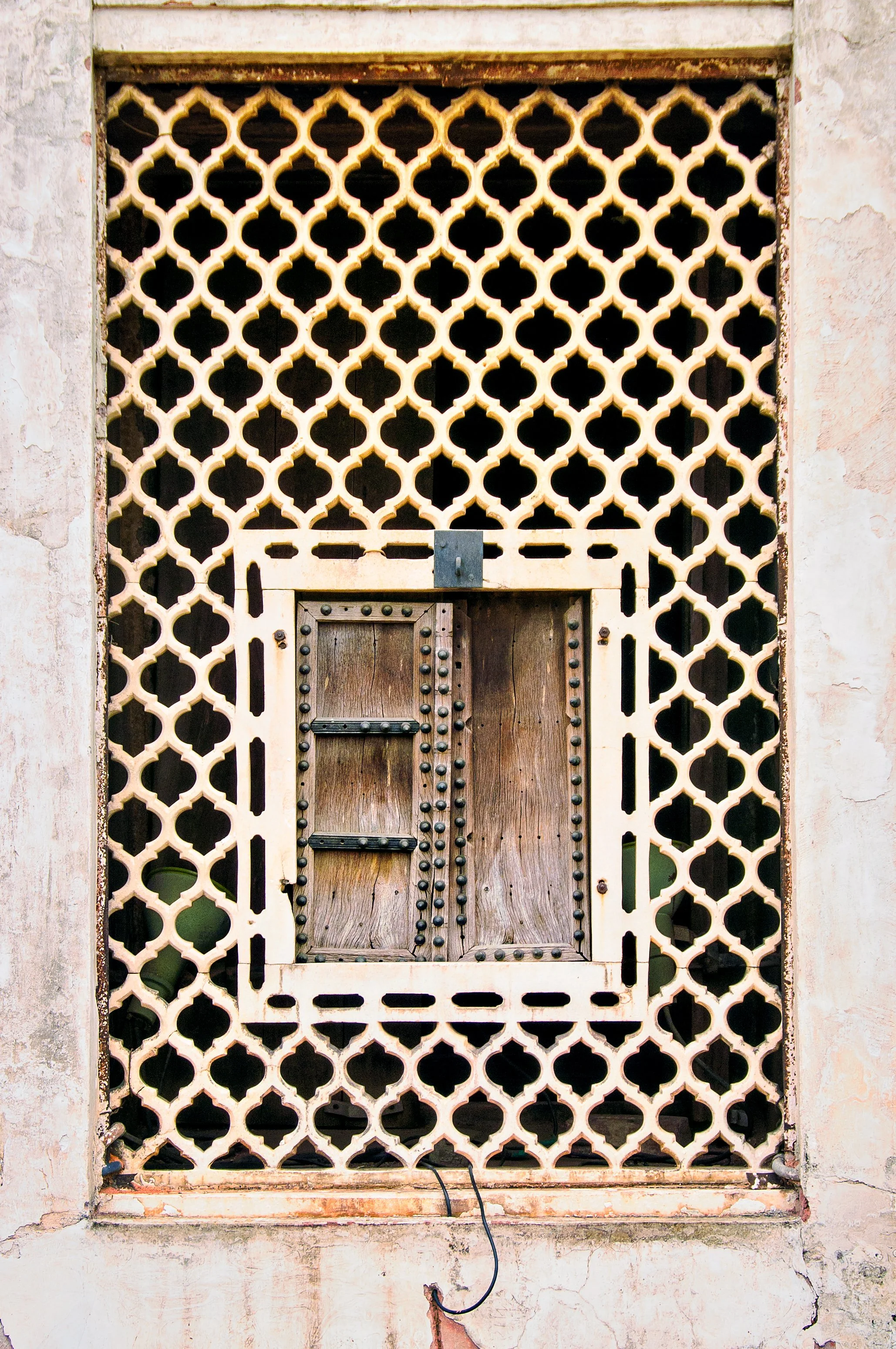 Decorative wall with a geometric pattern surrounding a small, boarded-up window with rivets.