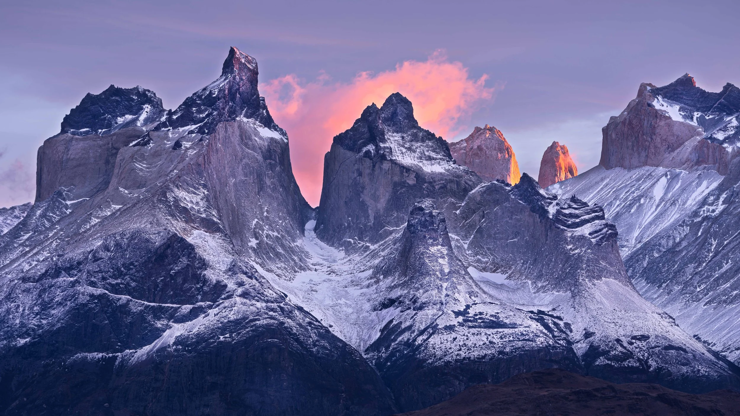 Snow-capped rugged mountain peaks during sunset with pink and purple sky.