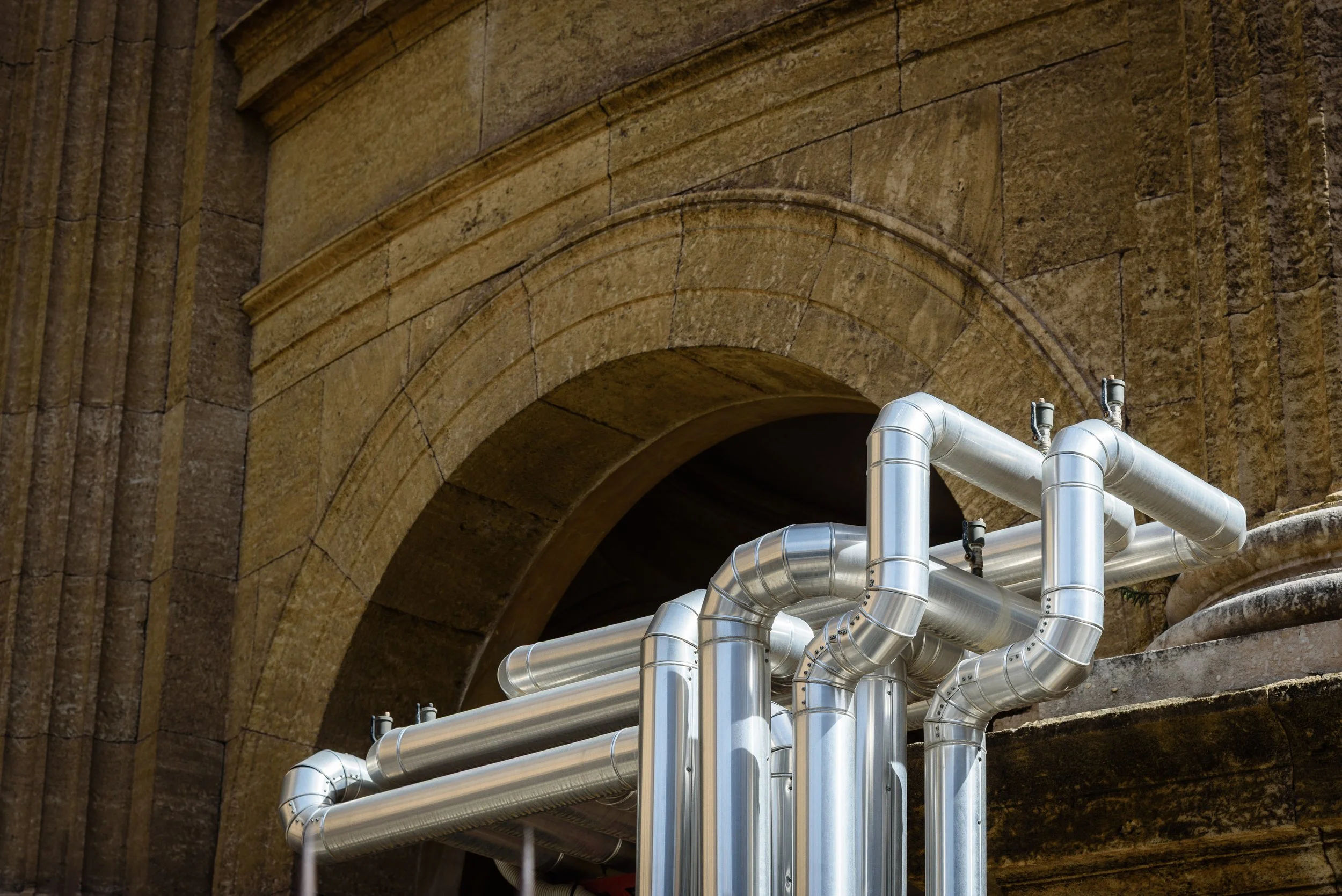 Silver industrial pipes connected on a stone building exterior.