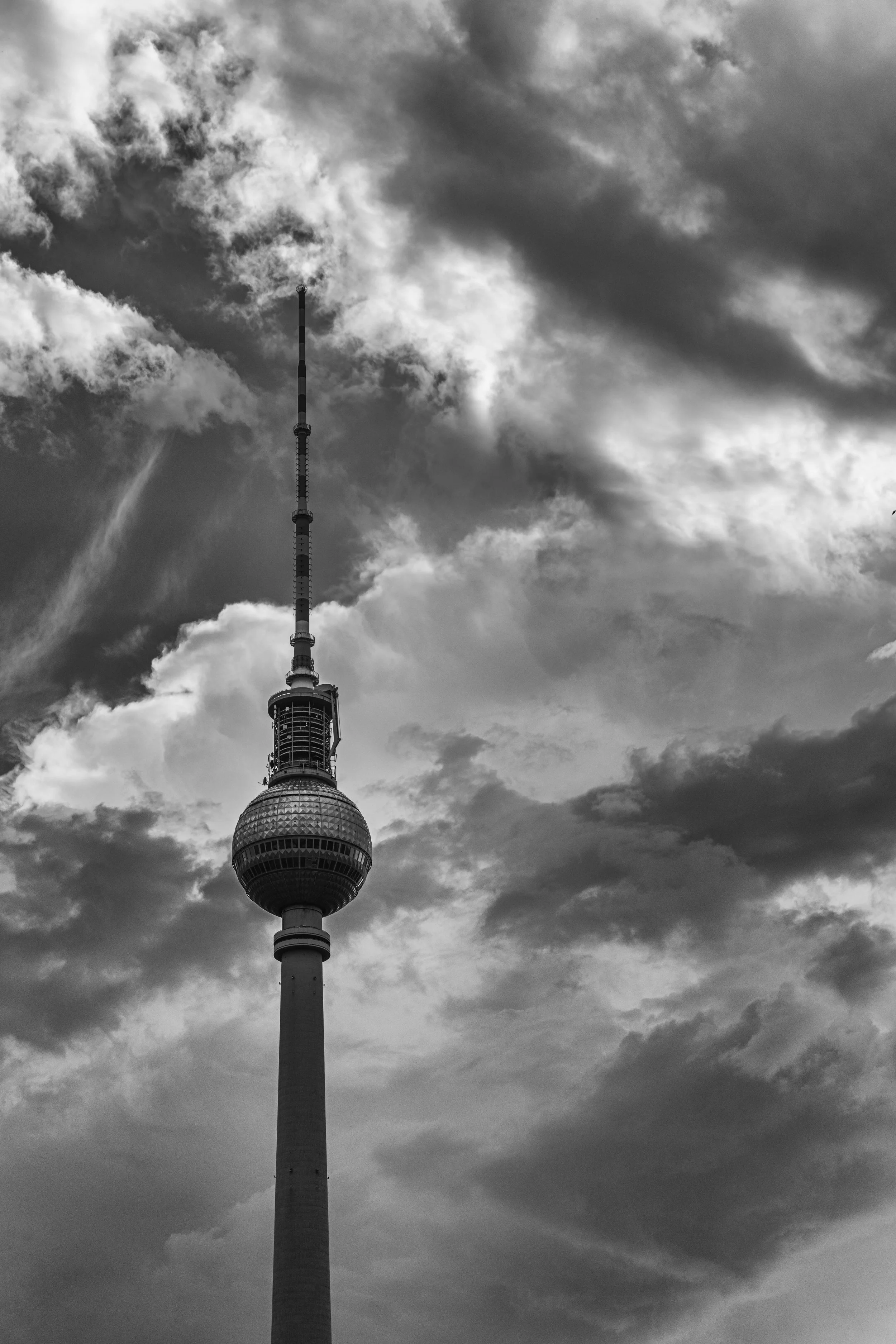 Black and white photo of the Berlin TV tower reaching into cloudy sky.
