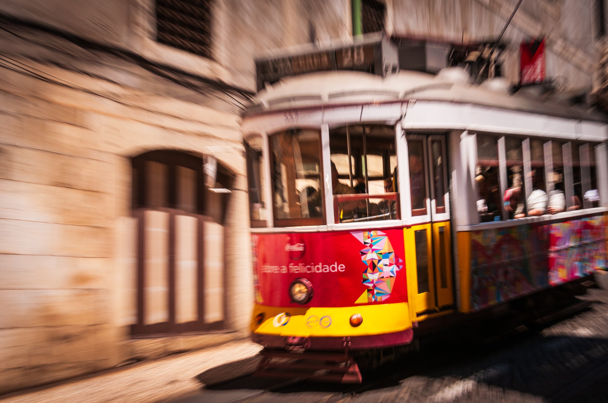 A colorful vintage tram moving along a street with stone buildings in the background.