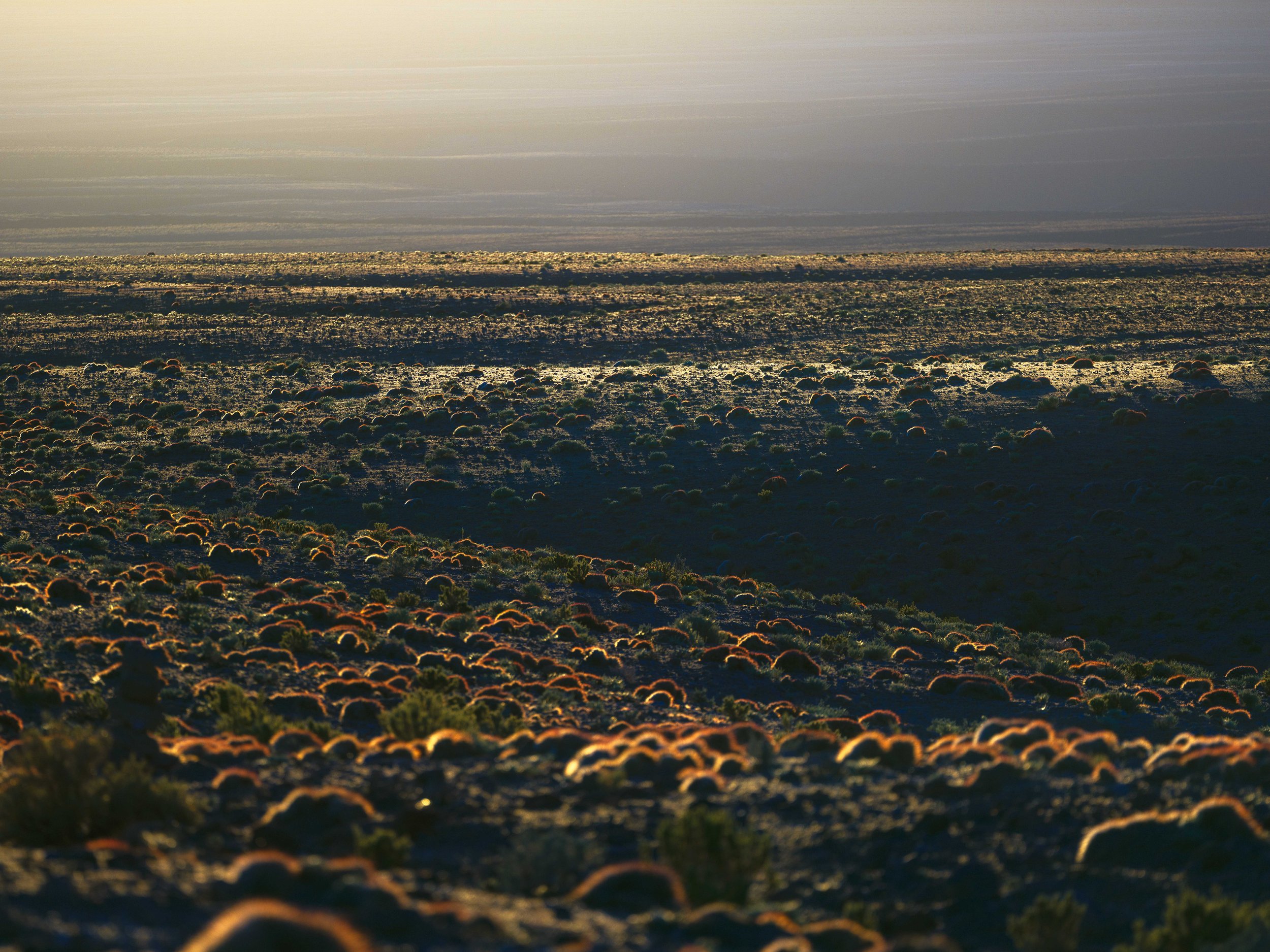 A desert landscape at sunset with rocky terrain and sparse vegetation