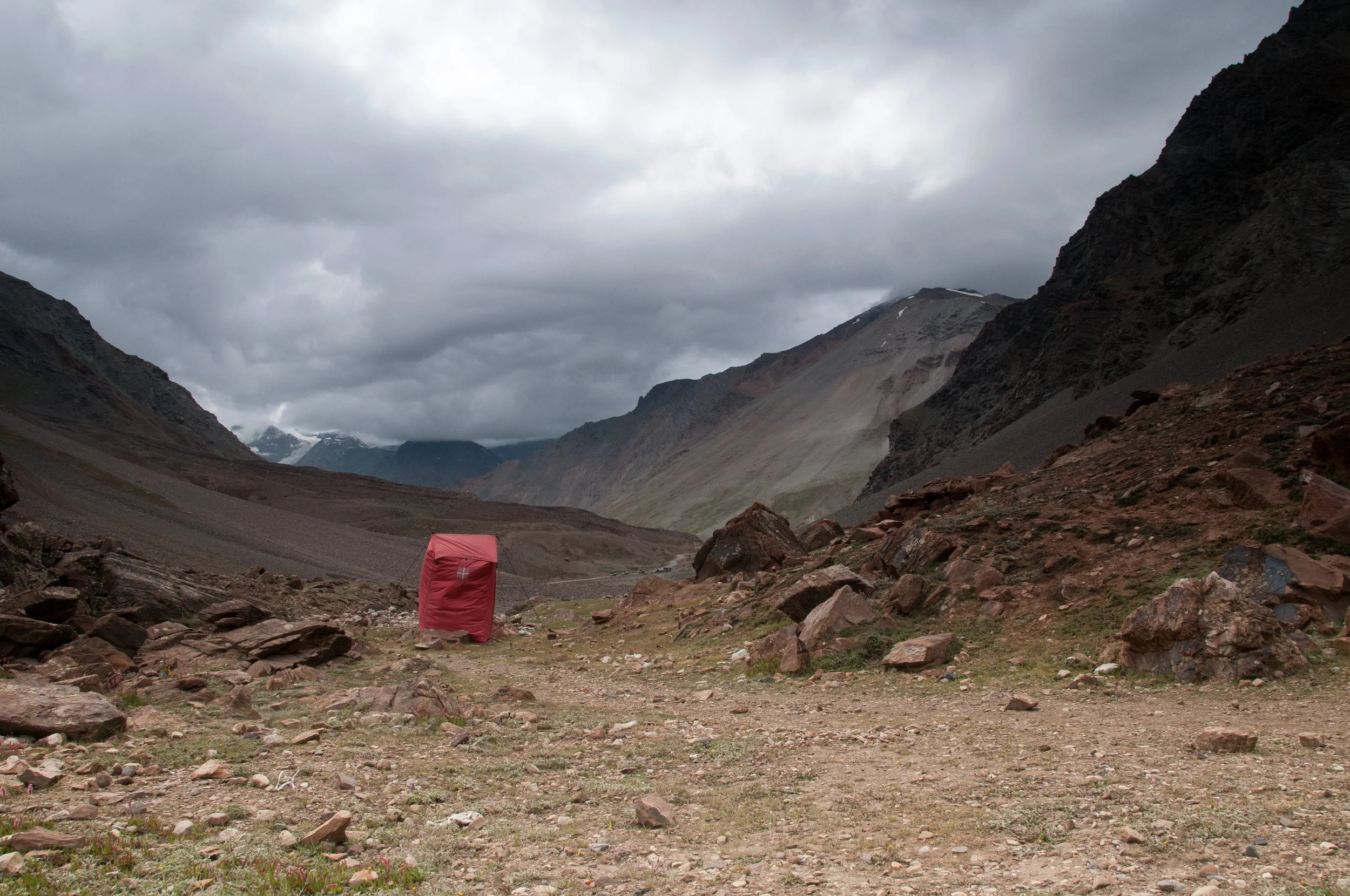 A solitary hovercraft on a rocky cleared area in a mountainous valley under cloudy skies, surrounded by rugged mountain slopes.