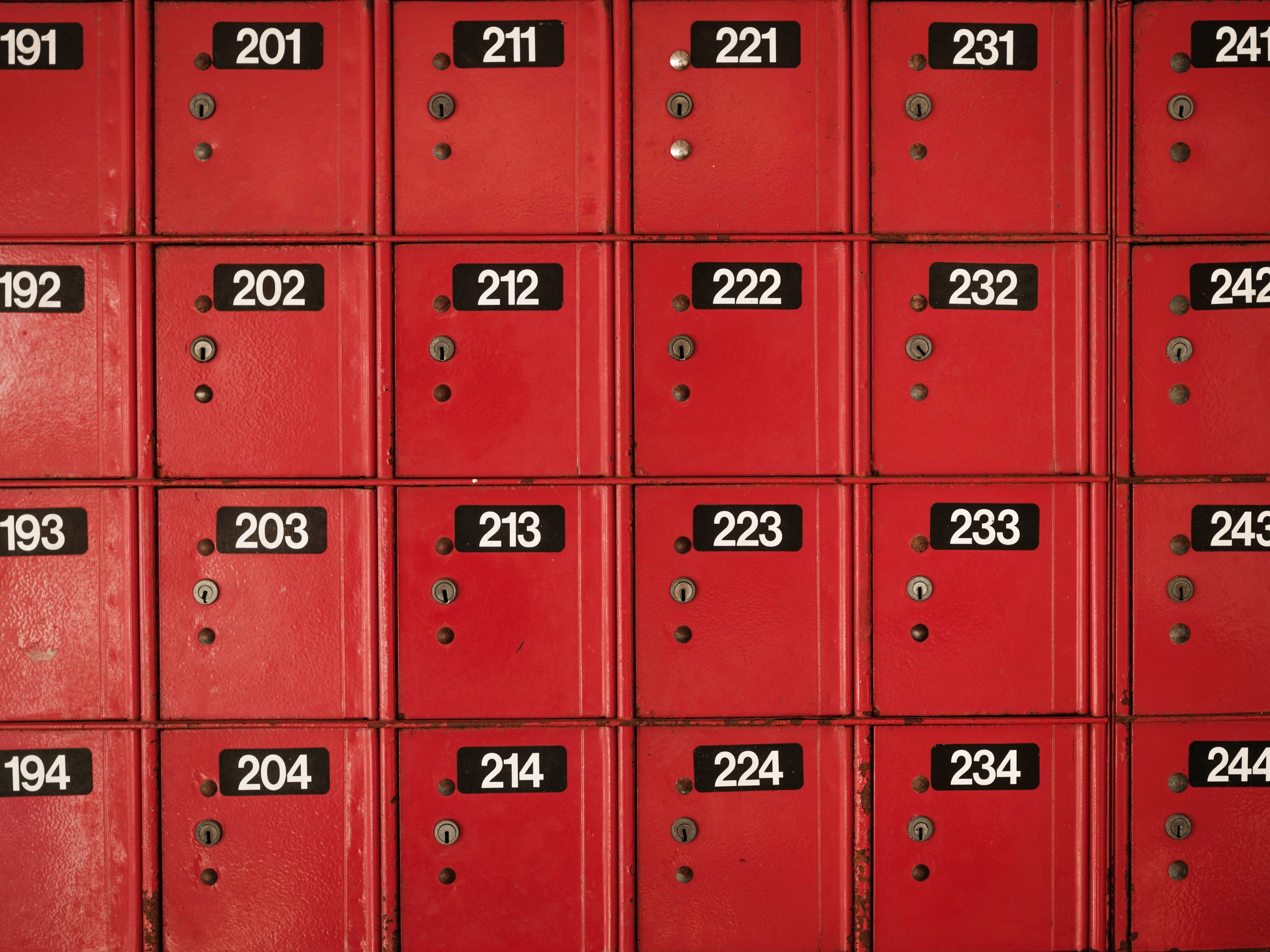 A row of red metal lockers with black and white numbered labels, including numbers 201 to 244.