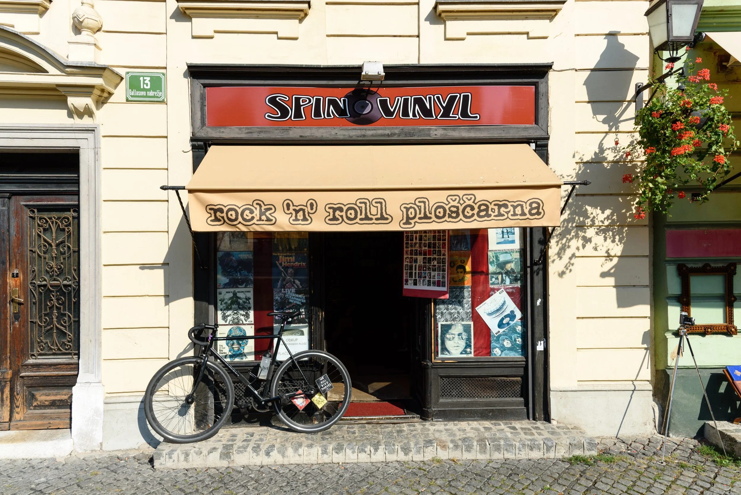 Storefront with a sign that reads 'Spin Vinyl' above an awning that says 'rock 'n' roll pioscanna.' Bicycle parked in front and posters inside window.